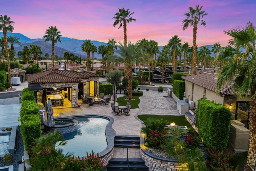 One of Motorcoach Country Club's most exceptional offerings. Lot 320 is an oversized, elevated corner water lot that feels like a double lot--yet with only one set of dues. Its unique positioning provides panoramic mountain views to the east and west, along with beautiful water views, all while offering an extraordinary level of privacy rarely found on a canal-front location.A large circular driveway, separate from the coach parking pad, provides abundant parking and includes the golf cart with your purchase. Beyond the private gated entry, the outdoor living space offers a large fire pit with seating for six, an overhead awning that provides shade and retains warmth, three permanently mounted cantilever umbrellas, a pop-up swivel TV, and an additional fire feature at the coach pad. The pool and elevated spa are exceptionally private and overlook the east canal and mountains. A custom staircase leads to your private dock, where an Electracraft boat--also included--awaits.Inside, bi-folding lanai doors open into the stunning 706 sq. ft. coach house. The chef's kitchen features a massive island with seating for six, under-counter wine fridge, reverse osmosis system, KitchenAid appliances, Wolf range with custom hood, full-size pantry with slide-out shelving, and hidden outlets for a seamless backsplash. The living area includes a linear Avanti fireplace, TV with soundbar, tinted glass, and electric drop screens discreetly built into custom soffits for shade and privacy. Double sliders open to an elevated private patio with mountain views, a drop-screen awning, and thoughtfully designed landscaping that provides privacy without obstructing scenery. The entire property is powered by a premium Control4 smart-home system managing lighting, music, shades, and more.The casita offers two wardrobes, a large built-in 180 bottle wine fridge, and a beautifully finished 3/4 bath with a full tile shower. Custom French doors open directly to the outdoor fire pit area. Additional storage and a full-size stacked washer/dryer are conveniently located inside for your convenience.Motorcoach Country Club is an exclusive, guard-gated Class A luxury motorcoach resort requiring coaches 30'-45'. Owners enjoy world-class amenities including golf, a 5-star clubhouse, fine dining at Top of the Falls, a yacht club, fitness center, three pools, tennis, pickleball, and over two miles of stunning waterways.