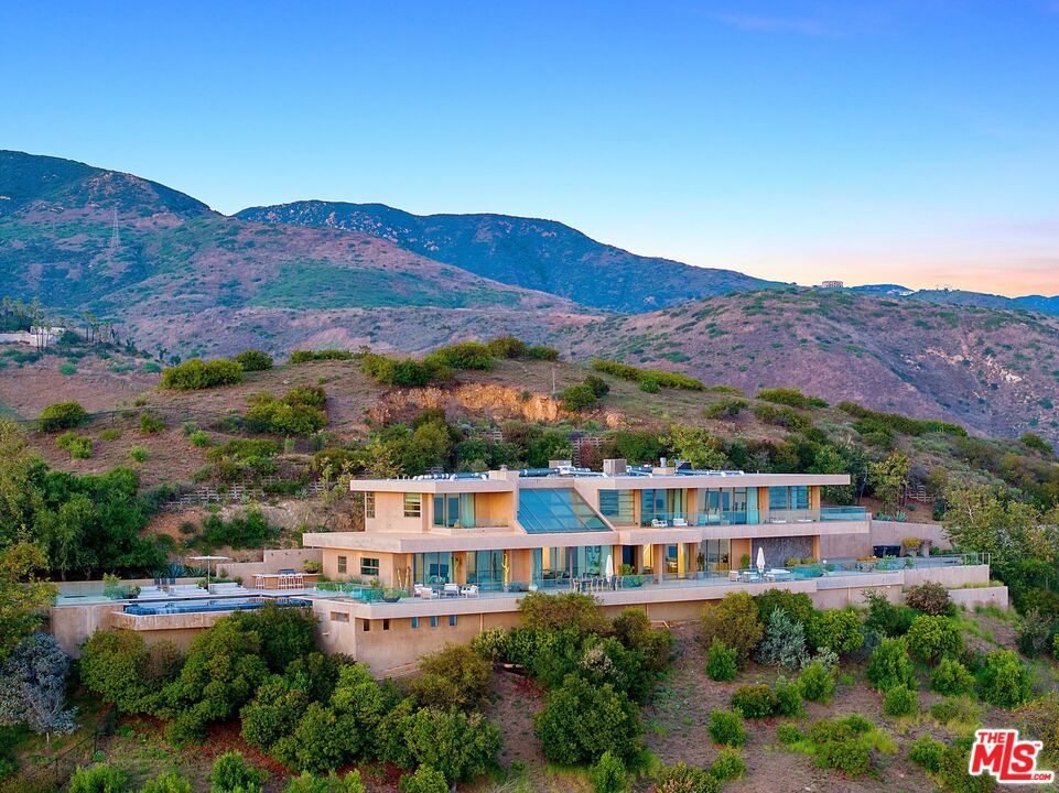 Nestled atop Winding Way in Malibu, spanning approximately 15.5 acres, lies an architectural gem crafted by the renowned Michael E. Barsocchini. This contemporary marvel showcases sweeping vistas of the ocean, stretching from Palos Verdes to Point Mugu. Upon the second gated entrance, a grand double-height foyer ushers you into a magnificent great room, adorned with a fireplace, retractable glass walls, and luxurious travertine flooring, all set against a backdrop of breathtaking views. The living space, dining area, kitchen, and media room seamlessly flow into one another and open onto an expansive deck running the length of the residence. A sophisticated floating walkway guides you to the master suite, a sanctuary complete with a fireplace, opulent bath, exercise/yoga room, bespoke closet, office, and a secluded deck overlooking the vast Pacific. Three further en-suite bedrooms offer stunning ocean panoramas. Outdoors, a meticulously manicured lawn complements the infinity pool, spa, and barbecue enclave. Beyond the pool lie trails that meander through the estate's upper acreage, inviting moments of nature immersion. Experience unparalleled sunsets from this designer haven perched in the Malibu hills. Please note total square footage includes basement
