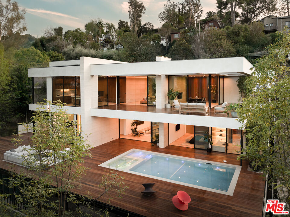 Nestled within the scenic hills of Studio City, 3748 Berry Drive is a testament to architectural brilliance and modern sustainability. This 6,264 sq.ft. net-zero masterpiece, crafted by Maison by PGB, seamlessly merges cutting-edge design with mid-century-inspired sophistication. Boasting 4 bedrooms, 4.5 bathrooms, a dedicated entertainment floor, private gym, and saltwater pool, the home offers not just breathtaking city views but a lifestyle defined by privacy and refined elegance. From the moment you step through the 10-foot glass pivot door, the home unfolds into an expansive, light-drenched sanctuary. Walls of multi-panel sliding glass doors erase the divide between indoor and outdoor living, while Moca Cream Portuguese limestone feature walls and brushed oak wide-plank flooring introduce warmth and timeless appeal. The chef's kitchen is a culinary marvel, featuring Taj Mahal Brazilian quartzite countertops, custom smoked walnut cabinetry accented with brushed brass, and state-of-the-art integrated Miele appliances. A stunning double-sided DaVinci fireplace delineates the living and dining spaces, inviting you onto a wraparound deck that frames unobstructed treetops and city views the perfect backdrop for entertaining or quiet reflection. The lower entertainment floor elevates hosting to an art form, complete with a custom bar adorned in Calacatta Gold Italian marble, polished concrete floors, and a dramatic smoked bronze mirror accent wall. Every bathroom feels like a private spa, with luxurious materials such as Cristallo Brazilian quartzite, Nordic Grey marble, and elegantly crafted brushed brass fixtures enhancing each space. True to its commitment to sustainability, the home features a photovoltaic solar array, grey water recycling system, and thermal-coated skylights for optimal energy efficiency. The outdoor spaces are equally captivating, with sprawling Ipe wood decks, a built-in BBQ island, and a shimmering 16' x 32' saltwater pool and spa, all embraced by lush, drought-tolerant native landscaping.