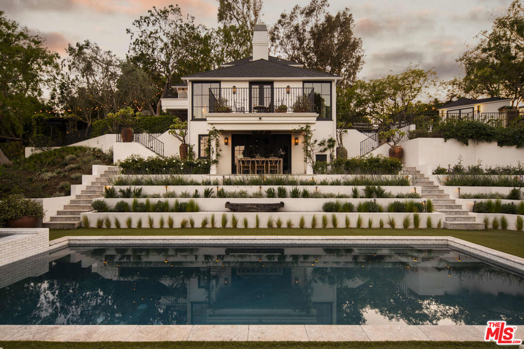 Perched on a quiet ridge in the Hollywood Hills, 7422 Palo Vista has been thoughtfully reimagined by Jake Arnold with landscaping by Trilling Landscape. The result is a refined and quietly expressive 3-bedroom, 4-bath home that balances natural textures, designer details, and elegantly framed views. Inside, rich materials - plaster walls, bespoke millwork, and organic stone - create a tactile, elevated experience. Each room flows effortlessly into the next, with natural light playing off warm tones and curated finishes. A formal living room with floor-to-ceiling windows frame the city beyond, while a sculptural stone fireplace brings intimacy to the open plan. The adjoining dining space and kitchen - anchored by a Calacatta Viola marble island and Lacanche range - lead directly out to a covered terrace complete with outdoor dining, a built-in BBQ, and a wood-burning pizza oven. Upstairs, the primary suite is a sanctuary unto itself, complete with a spa-like bath, steam shower and private balcony framed by panoramic views. Two additional bedrooms and a dedicated office structure provide flexibility for family or guests. Every room feels connected to the landscape, whether through verdant views, direct outdoor access, or generous natural light. Downstairs, a full-floor entertaining level offers a custom screening room that opens up to a serene dining area. Surrounded by mature hedges and layered greenery, the outdoor spaces are designed for quiet moments and effortless entertaining alike.
