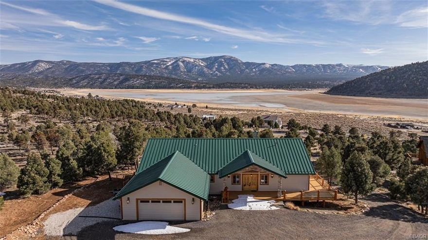 Soak in breathtaking panoramic views of the San Bernardino Mountains, ski slopes, and Baldwin Lake from this stunning single-story retreat. Designed with soaring vaulted ceilings and an open floor plan, this home features expansive windows that frame the beauty of Big Bear Valley. With four en-suite bedrooms, each offering a cozy freestanding fireplace, your guests will feel welcomed and at home. The primary suite, thoughtfully positioned for privacy, boasts a luxurious jetted bathtub with unobstructed views and a relaxing sauna. The chef's kitchen is designed for effortless entertaining, complete with granite countertops, dual microwaves, ovens, and sinks. A charming breakfast nook provides the perfect spot to enjoy your morning coffee while taking in the serene surroundings. Step outside onto the partial wraparound Trex deck, where you can immerse yourself in nature. Nestled on a sprawling 70,131 sq. ft. lot that adjoins the National Forest, this property offers unmatched tranquility and seclusion. Practical features include a well and two 500-gallon water tank for fire suppression, ensuring both comfort and peace of mind. Experience the perfect blend of luxury, functionality, and breathtaking scenery in this one-of-a-kind mountain retreat.