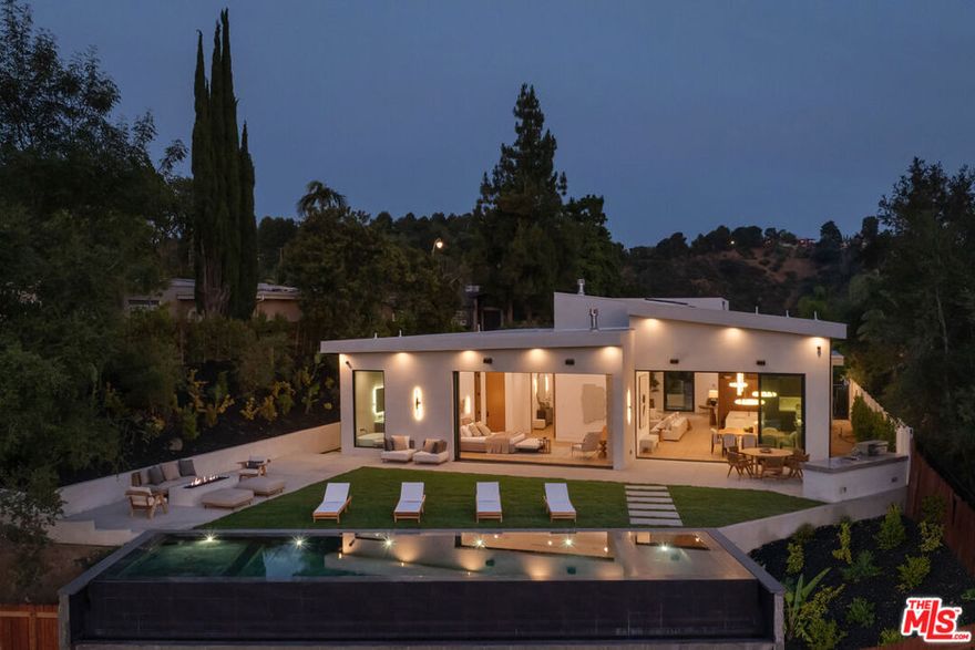 Tucked away on a quiet cul-de-sac in the prestigious Beverly Hills Post Office area, this newly completed modern masterpiece offers breathtaking jetliner canyon views. Privately gated for maximum security and seclusion, the home showcases soaring 18-foot mahogany-clad ceilings, multiple skylights, a dramatic 16-foot-tall library, and expansive sliding glass doors for seamless indoor-outdoor living. The dramatic black-tiled pool, perched on five structural caissons, features a stylish Baja shelf - perfect for lounging in privacy while enjoying the view. Distinctive interior finishes include white oak flooring, Calacatta Cremo countertops in the kitchen, Fantasy Pink marble vanities in the guest suites, and a powder room with Calacatta Picasso marble and Roman clay walls. Custom walnut cabinetry adds warmth and sophistication throughout. The primary suite features a serene sitting area, a large custom walk-in closet, and a spa-like bath with a soaking tub overlooking the stunning views. Outdoors, enjoy a full kitchen equipped with a sink, BBQ, and refrigerator, along with a built-in fire pit perfect for entertaining. Every detail has been thoughtfully curated to elevate both design and function. With world-class finishes and exceptional craftsmanship, this home is a true expression of luxury living.
