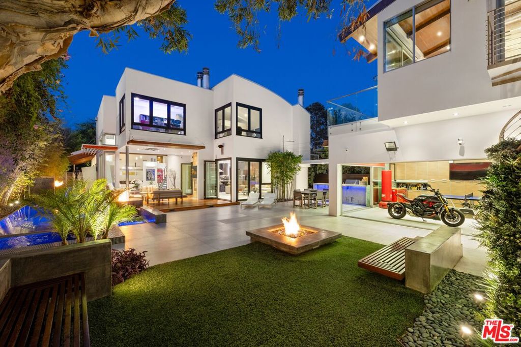 Concealed from the street by lush landscaping and mature trees, this exquisite contemporary entertainer's compound offers a variety of modern amenities and a private, zen lifestyle in a coveted North of Montana neighborhood. Guests arrive past a variety of plantings, art pieces, and calming water feature, unaware of the many surprises that await. Inside, floor-to-ceiling picture windows and sliding glass invite natural light into the formal living room with its lofty double-height ceilings, exposed wood beams, dramatic staircase, and wet bar. A pocket door retreats to provide seamless flow into the outdoor living room with built-in heating, decorative fireplace, and fire pit adjacent to the sparkling black-bottom pool and spa. Designed with quintessential California living top of mind, the nearby formal dining room also opens to the home's peaceful bamboo-lined grounds. The custom Italian chef-grade kitchen is complete with state-of-the-art appliances including Wolf range with pot filler and Miele warming drawer as well as a retractable flat screen and waterfall island. The adjacent family room also opens to the outside and features a massive 115-inch TV. The primary suite includes a large Vegas hotel-inspired bathroom with two large vanities, steam shower, and jetted tub plus an en-suite office. Secondary bedrooms and bathrooms are light-filled and have modern finishes. In the backyard, discover a spectacular two-story converted garage that can house vehicles or be used as a rec room, billiards, and more. On its second level is a gym, yoga, or artist's studio plus rainwater shower and an oversized glass-encased steam room. There is also a built-in barbecue and outdoor dining, a large amount of patio space, and a sitting area with a second fire pit for evening conversation. Welcome to this prime location near the Brentwood Country Club and Country Mart, just moments to the area's top-rated restaurants, schools, parks, golf courses, shopping, and world-class beaches.