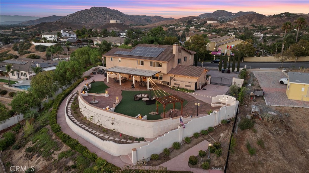 SELLER OPEN TO PROVIDING A CREDIT TOWARDS INTEREST RATE BUY DOWN. Inquire for more details. Nestled within the tranquil confines of Norco Hills, this exquisite estate exudes sophistication, class and a touch of Tuscany-country charm. Spanning 3,895 square feet of living space on a sprawling .87-acre lot, this gated residence offers unparalleled privacy and unobstructed, panoramic city-light and mountain views. As you approach the property, you’ll be captivated by the meticulously designed exterior, surrounded by stucco-finished block walls, iron fences, and a remote-control gate that leads to a paved front entrance. The impressive entryway through the gated courtyard is adorned with lush vines wrapped around the archway, guiding you to the custom wrought iron double doors. Step inside to soaring two-story ceilings and be greeted by the luxurious board and batten walls, complemented by rich hardwood flooring and pristine tile. The ornate wrought iron staircase is a masterpiece. The gourmet kitchen is a chef’s dream, featuring a large island with bar seating, granite countertops, a built-in gas range and hood, and stainless-steel appliances. This space seamlessly flows into the family room, where French doors open to the breathtaking tri-level backyard. Completing the main level is an office that can be converted into a 5th bedroom plus a bathroom with a standing shower, as well as, a powder bathroom perfect for accommodating guests. Upstairs, the massive primary suite is a sanctuary, offering more of those incredible views. The spa-like primary bathroom boasts his and her walk-in closets, dual sink vanities with granite countertops, marble flooring, a tumbled travertine soaking tub, and a spacious walk-in shower with a rainfall showerhead. An additional three generously sized secondary bedrooms can be found upstairs featuring mirrored closets. There is also an upstairs hallway bathroom with dual sinks, granite countertops and a shower tub. The outdoor space is nothing short of spectacular, with a built-in BBQ counter, 2 fireplaces, 5 gas fire pits, 2 water fountains, 3 chicken coops, various fruit trees, and designated planters to grow your own food. Enjoy al-fresco dining while viewing incredible sunset views under the Alumawood-covered patio with 3 ceiling fans. Additional features include a spacious laundry room with extra storage, double 2-car garages accommodating up to four vehicles, and a long gated driveway for RV parking. Paid off solar and no HOA!