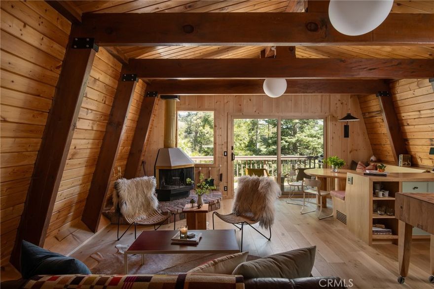 A uniquely custom cabin that pairs a quiet architectural presence with a rich interior palette and is enveloped by a lush environment, defined by craftsmanship and intention. Set beneath a distinctive gambrel roof, the residence offers a welcoming blend of warmth, texture, and high-end detailing throughout. Exposed wood beamed ceilings bring a sense of grounded elegance to the living room, where the original corner fireplace creates intimacy among the the flow of the space. Anderson wood-clad windows allow natural light to pour in, illuminating the home's curated finishes. The kitchen is a standout—anchored by honed Basaltina countertops and accented white oak cabinetry, with a Thor range and Retro Mod refrigerator offering a mix of modern performance and vintage styling. Fixtures include Brizo’s Odin faucets chosen for their sculptural minimalism. Zia tile backsplash adds a refined layer of texture and tone. A multi-functional banquette with white oak bench seating and custom cushions—upholstered in Perennials’ Raffia fabric by Legacy Custom Upholstery—adds thoughtful utility and charm. The main level features a Clé cement tile powder room adding artisanal character. Downstairs, the primary suite sits within the mature foliage,  featuring a large picture window that frames the verdent exterior, creating a peaceful, light-filled retreat. A jewel box style bathroom is wrapped in mint penny tile, with a custom terracotta vanity. An additional cozy wood clad guest room is tucked in adjacently. Throughout the home, walls and closet doors are wrapped in flat-planked pine, echoing the warmth and texture of the exposed ceilings. The floors are finished in Vandyck wood, grounding the entire home in a natural, cohesive palette.  A lower level expansive deck acts a second living space, and is shaded within the surrounding Dogwood, Cedar and Pine trees while an upper level balcony allows for an airy tree top experience with horizon views.  Every element has been considered—from materials and hardware to color and form—to create a space that feels both elevated and deeply livable.