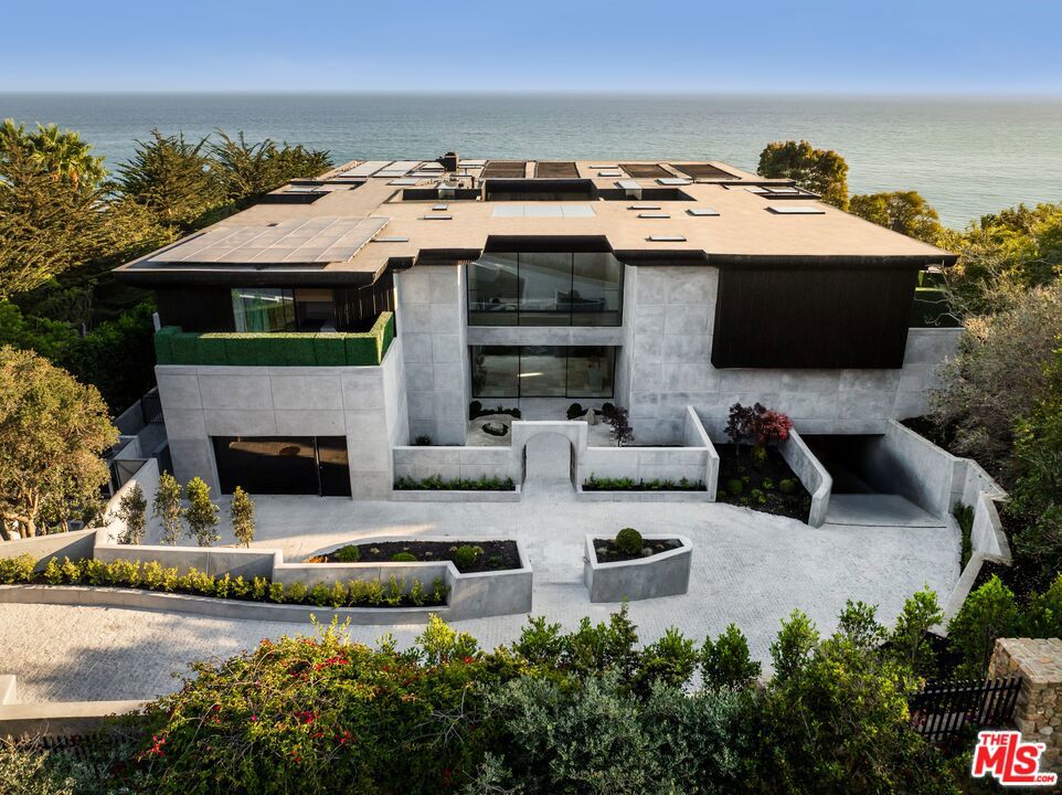 There are homes you live in and there are homes that live forever. Welcome to Simka Malibu - an awe-inspiring creation by "God's Architect" Kris Halliday. Thirty thousand square feet of architectural permanence rising from the bluffs of the Pacific, conceived as both fortress and sanctuary. A location chosen with the foresight of a thousand years thoughtfully positioned, engineered, and constructed with resilience in mind - designed to meet the challenges of fire, earthquake, tsunami, mudslide, and storm erosion. Built with over 7,300 cubic yards of super-reinforced concrete, Simka is a monument to permanence. Every line, every proportion, every material was shaped by one mind, one vision, one creation. The result is not just architecture, but a living work of art. Defined by bold lines of concrete and glass, softened by sculptural landscaping and curated natural stones from around the world, the estate embodies GA's philosophy of Brutality Vitality - where strength is balanced by serenity, and concrete itself is reimagined into a velvet-like presence. Entry unfolds through a secondary gated entry into a tranquil zen courtyard and stone pathway, revealing interiors where floor-to-ceiling glass dissolves the boundary between home and horizon. Simka is a sanctuary - built on Divine Masculinity, created to protect, nurture, and heal. Life here unfolds through sublime experiences: a 176-foot multi-level vein-matched stone pool with swim-up bar, sunken lounge, and dramatic viewing window merging seamlessly with the Pacific horizon. A world-class theater with a 235-inch LED screen, Dolby Atmos sound, and Atelier Italian leather recliners rivals the world's finest private cinemas. A Japanese tea room - a sanctuary within the sanctuary - offers profound quiet. The full commercial kitchen easily supports gourmet cooking for up to 200 guests, complemented by terraces for al fresco dining, shaded loggias, and an outdoor kitchen for endless gatherings. Throughout, water and nature flow: Japanese gardens, waterfalls, meditation courts, koi ponds, and pathways that weave stillness into daily life. Swinging daybeds, a circular fire lounge, and open-air courtyards transform relaxation into ritual. For wellness and longevity, Simka offers a full spa, cold plunge, sauna, treatment rooms, and a state-of-the-art gym with underwater pool windows. A nightclub, private guest suites, and an underground 10-car garage complete the lifestyle offering. The 1,800 sq ft primary suite is a private sanctuary suspended above the waves, with its own hot tubs, fireplace lounge, and spa-inspired bath. Additional suites echo this intimacy, blending organic textures, curated furnishings, and panoramic ocean views. Every detail, down to marble-clad powder rooms designed as art, speaks to permanence and intention. With 10 bedrooms, 20 bathrooms, and seamless indoor-outdoor living, Simka is monumental yet intimate - enduring yet ethereal. Not built for a decade or a generation, but for centuries. Simka Malibu - architecture for eternity.