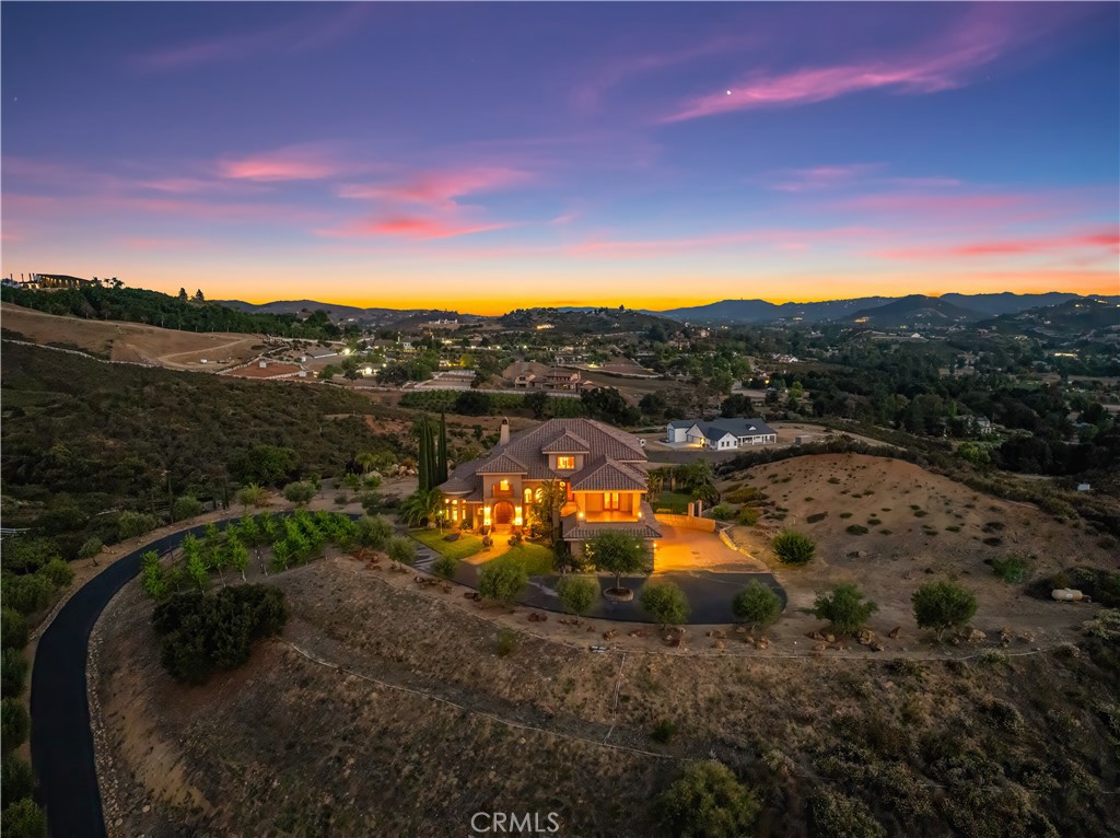 Welcome to your hilltop haven in the heart of La Cresta—where peace, privacy, and sweeping vistas surround you on five sun-drenched acres. This gated Tuscan-inspired estate feels like a world apart, offering the perfect blend of timeless charm and modern, sustainable living. Thoughtfully designed for comfort and style, this high-end custom home lives like a single story, with the spacious primary suite conveniently located on the main level. Step inside to a dramatic grand entry, soaring ceilings, solid mahogany doors, and a wide-open floor plan finished with hardwood and travertine floors. The chef’s kitchen, adorned with custom granite countertops, flows seamlessly into the living and dining spaces—perfect for gatherings or quiet evenings by the fire. All four bedrooms feature private en-suite bathrooms, with two offering relaxing jetted tubs—ideal for unwinding after a long day. An elevator connects every level with ease, and over 1,500 square feet of scenic view decks invite you to sip wine, watch the sunset, and take in the fresh mountain air. This property is more than just beautiful—it’s functional, too. Enjoy energy independence with owned solar and a private well, giving you the freedom to live comfortably and sustainably. Whether you dream of farm-to-table living or simply appreciate peace of mind, this estate is a rare find. Wine lovers will appreciate the 500-bottle, temperature-controlled wine cellar, accessible from both the dining room and garage. Mature Syrah vines and 50 fruit-producing olive trees line the driveway, with additional fruit trees and irrigated space for gardens or future orchards. There’s even room to add an infinity-edge pool or additional structures. Equestrians will love the lower-level fenced corral with a horse stall, tack room, turnout area, and direct access to nearby riding trails—ride right from your own property! This is more than a home—it’s a peaceful retreat, a vineyard lifestyle, and a chance to live off the grid without sacrificing luxury.