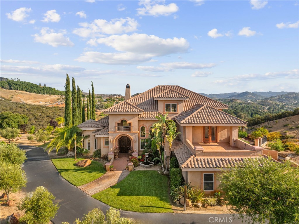 Welcome to your hilltop haven in the heart of La Cresta—where peace, privacy, and sweeping vistas surround you on five sun-drenched acres. This gated Tuscan-inspired estate feels like a world apart, offering the perfect blend of timeless charm and modern, sustainable living. Thoughtfully designed for comfort and style, this high-end custom home lives like a single story, with the spacious primary suite conveniently located on the main level. Step inside to a dramatic grand entry, soaring ceilings, solid mahogany doors, and a wide-open floor plan finished with hardwood and travertine floors. The chef’s kitchen, adorned with custom granite countertops, flows seamlessly into the living and dining spaces—perfect for gatherings or quiet evenings by the fire. All four bedrooms feature private en-suite bathrooms, with two offering relaxing jetted tubs—ideal for unwinding after a long day. An elevator connects every level with ease, and over 1,500 square feet of scenic view decks invite you to sip wine, watch the sunset, and take in the fresh mountain air. This property is more than just beautiful—it’s functional, too. Enjoy energy independence with owned solar and a private well, giving you the freedom to live comfortably and sustainably. Whether you dream of farm-to-table living or simply appreciate peace of mind, this estate is a rare find. Wine lovers will appreciate the 500-bottle, temperature-controlled wine cellar, accessible from both the dining room and garage. Mature Syrah vines and 50 fruit-producing olive trees line the driveway, with additional fruit trees and irrigated space for gardens or future orchards. There’s even room to add an infinity-edge pool or additional structures. Equestrians will love the lower-level fenced corral with a horse stall, tack room, turnout area, and direct access to nearby riding trails—ride right from your own property! This is more than a home—it’s a peaceful retreat, a vineyard lifestyle, and a chance to live off the grid without sacrificing luxury.