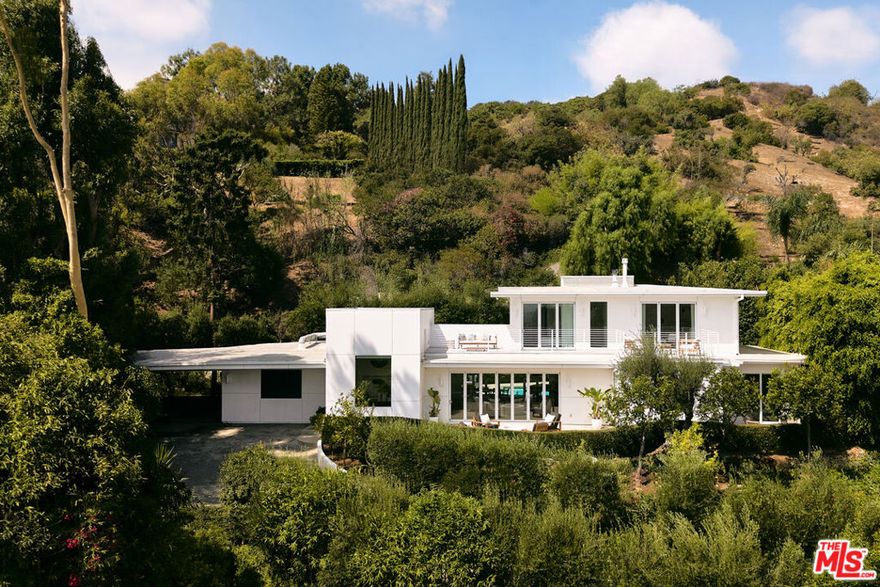 Tucked away in the prestigious Outpost Estates, this extraordinary residence offers a unique blend of organic modern style, breathtaking views, and ample privacy. Perched above the street behind gates and up a long driveway, this chic and understated home sits on an oversized lot enveloped by lush landscaping, creating a secluded sanctuary just moments from both the Westside and the San Fernando Valley. Expansive accordion-style walls of floor-to-ceiling glass frame sweeping city and canyon vistas, filling the interiors with natural light and a sense of openness. The seamless indoor-outdoor flow is enhanced by abundant outdoor living areas and a resort-like pool with hot tub, perfect for both intimate relaxation and large-scale entertaining. The open floor plan unites the family room, dining room, and chef's kitchen, where a generous island with bar seating and a pass-through window connects directly to a poolside bar. Folding glass doors on both sides of the main living areas create a remarkable sense of continuity between indoors and out. Each of the four bedrooms is a private retreat, complete with en-suite baths and direct access to outdoor spaces. The luxurious primary suite boasts a spa-like bathroom with soaking tub, dual rain shower, and an ample walk-in closet. Additional amenities include a state-of-the-art professional music studio, glass-enclosed wine cellar, and multiple fireplaces and firepits. Modern, elegant, and designed for effortless California living, this is a rare offering in one of Los Angeles' most coveted neighborhoods.