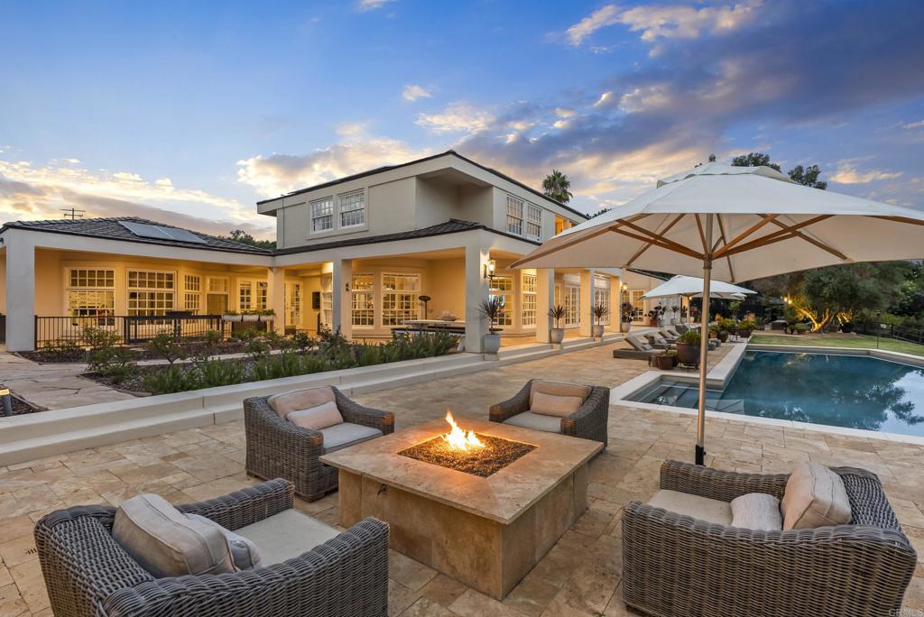 Behind private gates in the heart of the Rancho Santa Fe Covenant, this timeless estate offers the perfect blend of sophistication, comfort, and resort-style living on two pristine acres. With 7,717 square feet of living space, the property encompasses a 5-bedroom, 5.5-bath main residence and a detached 1bed/1bath guest casita, surrounded by lush landscaping and expansive grounds designed for both privacy and entertaining. Inside, the home’s modern traditional design combines classic craftsmanship with warm, inviting spaces. Soaring ceilings and an open floor plan create a natural flow, while large-scale windows and French doors frame garden views and bring the outdoors in. Formal living and dining spaces are balanced by casual gathering areas, including a game room with a bar, designed for effortless entertaining. The gourmet chef’s kitchen—complete with butler’s pantry, multiple ovens, and a sunny breakfast nook—opens to the family room, where mornings and evenings alike are centered around connection. The first-floor primary suite commands its own private wing, featuring a sitting area with fireplace, French doors to a covered loggia, dual dressing rooms, and a spa-inspired bath. Upstairs, three additional en-suite bedrooms are joined by generous lounge areas and a bonus room, creating the ideal retreat for family or guests. Outdoors, the property transforms into a private resort. A sparkling pool and spa are complemented by multiple firepits, a covered outdoor living/dining room, and an outdoor kitchen. Olive trees strung with lights create enchanting spaces to gather, while the greenhouse and gardens offer opportunities for homegrown produce. With wide lawns, fragrant rose gardens, and a serene southern view, every corner of the estate is designed to be enjoyed. Additional amenities include solar power, garaging for four cars, and direct access to Rancho Santa Fe’s trail system. Just minutes from the Village, golf, tennis, and top-rated schools, this Covenant estate captures the essence of refined living in one of Southern California’s most sought-after communities.