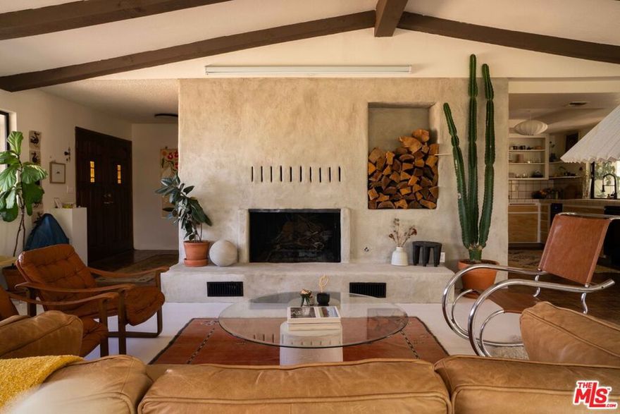 The House on Joshua Lane. South of the highway towards the end of the road you'll find this sweet Spanish villa just outside of Joshua Tree National Park. This 1980's home in upper Sky Harbor still has cool original elements like a dramatic floor-to-ceiling fireplace, sun room that stretches along the length of the home with over 200 square feet of space and a very 80's stone brick wall bathroom. All the while, it's been upgraded in all the right places. Meticulously loved and renovated, the large double front door opens into a proper entry way that splits the living space and the rest of the home. Go left and get swept up by the vaulted ceiling with exposed beams and an expansive living area. The fireplace commands your attention; refinished with a concrete overlay, a built-in bench and fire log display; it becomes the focal point of the room. The living room has been thoughtfully arranged to have multiple spaces. Cozy up around the fireplace or watch movies on the mounted projector, move to the seating area to dive into a good book or listen to a record, or make yourself a drink at the built-in drybar. The kitchen has been refreshed with new cabinet faces, new appliances, and open shelving. The window behind the sink opens to bar seating inside the enclosed sunroom, a fun hosting feature for your friends! The open concept allows for plenty of space for a dedicated dining area or take it outside for alfresco meals under the covered patio. On the other side of the home you'll find two spacious guest bedroom, guest bathrooms, and the expansive primary suite. The primary bedroom is on the south side of the home with sliding glass doors to the enclosed patio, a full bathroom with double sinks plus a large walk-in closet. Find the half bath in the entry hallway with an unforgettable stone brick wall, upgraded lighting fixtures and Moroccan tile. There is an intuitive flow around the home making it the perfect place to host or welcome a full family. The property is fully fenced and situated on the lot for privacy and beautiful sunrise and sunset views. The home is surrounded by mature shade trees that help keep the lot cool plus a new HVAC system. There is an attached two car garage with laundry, tankless water heater and storage as well as a large RV garage toward the back of the 1.4 acre lot. Joshua Lane is perfectly placed for convenient access to everything in Yucca Valley or Joshua Tree while still feeling like the perfect desert retreat. You're just 10 minutes to The Copper Room, Tiny Pony + Desierto Alto, Frontier, The Dez, and so much more.