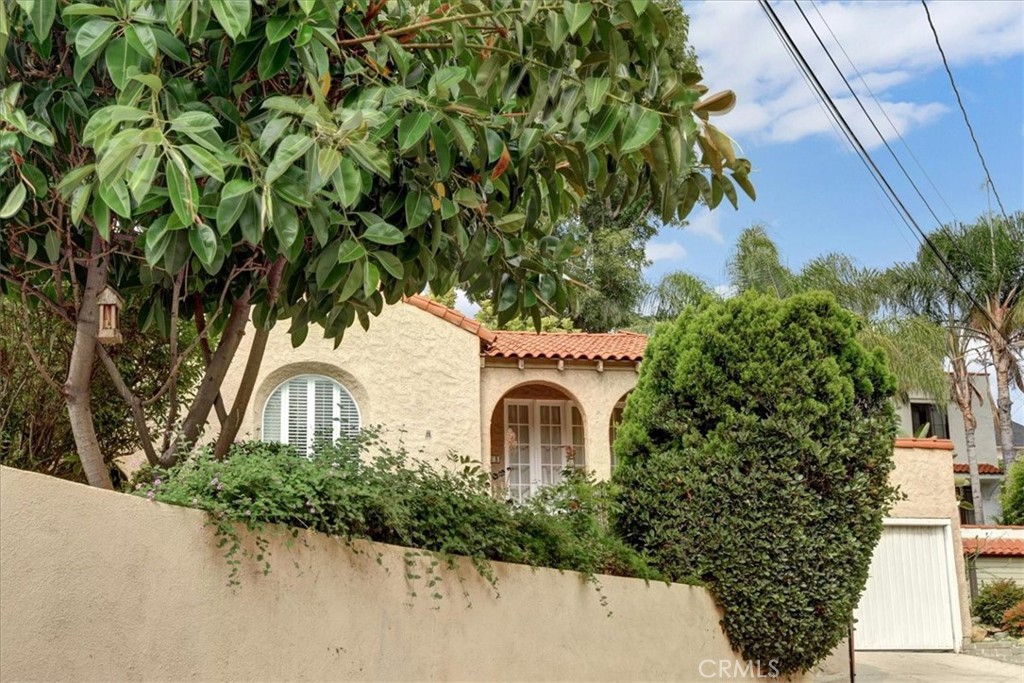 Tucked behind lush, mature landscaping, this charming single-story residence blends timeless character with thoughtful functionality. Spanning over 1,200 square feet, the home features a split-level layout that introduces a sun-drenched living room adorned with a classic fireplace, graceful archways, and hardwood floors that flow seamlessly throughout. The separate dining room opens directly to the backyard through sliding glass doors, creating an effortless connection between indoor comfort and open-air living—ideal for both everyday enjoyment and entertaining.
The kitchen retains its vintage appeal, featuring stainless steel appliances and a Dutch door that also leads to the serene backyard retreat. A front-facing rooftop patio provides an inviting setting for morning coffee, quiet afternoons, or evening sunsets. The home offers two well-proportioned bedrooms and one full bathroom, along with a secondary bath—equipped with a shower and sink—conveniently adjoining the primary bedroom. A beautifully adaptable second bedroom offers endless possibilities, ideal for guests, a home office, or a creative studio. Additional highlights include a two-car garage, offering both secure parking and additional storage. Ideally situated in one of Los Angeles’ most desirable neighborhoods, this Los Feliz gem is just moments from the vibrant shops, dining, and cultural scene of nearby Silver Lake.