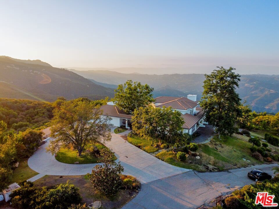 Perched atop a private promontory with commanding, unobstructed views of the Pacific Ocean, the Queen's Necklace, Catalina Island, and the glittering skyline of Los Angeles, 21965 Saddle Peak Road is a rare architectural offering in one of Topanga's most exclusive and private neighborhoods. This singular estate presents a refined vision of California living where timeless design, panoramic vistas, and indoor-outdoor flow converge in harmony. The home is a single-level hacienda of approximately 4,250 square feet, thoughtfully laid out and filled with natural light. Towering 20-foot ceilings in both the formal living room and the library create a feeling of spaciousness and quiet grandeur, while oversized windows capture sweeping coastal and city views that evolve throughout the day. Ideal for the art collector, the home offers gallery-style walls and dramatic scale, creating an inspiring backdrop for personal expression. Rich hardwood floors run throughout the interior, grounding the space in warmth and elegance. A well-proportioned media and family room adds versatility, while a screened-in garden room with a view invites relaxed evenings immersed in nature without sacrificing comfort. The open-concept chef's kitchen is designed for both everyday functionality and entertaining at scale, flowing seamlessly into adjacent living and dining spaces and out to the expansive covered patios beyond. Every room is oriented to maximize light and views while maintaining a sense of privacy and calm.The luxurious primary suite is its own retreat within the home, offering a serene vantage point over the surrounding landscape. With dual walk-in closets, a deep soaking tub, and separate vanities, the suite is a space designed for rest, renewal, and quiet indulgence. Two additional bedrooms, thoughtfully positioned, provide comfort and privacy for family or guests.The grounds are as carefully considered as the interiorsfeaturing broad rolling lawns, mature landscaping, a secret garden, and a micro-vineyard that nods to the romance of wine country living. Generous outdoor entertaining areas, including large covered patios, invite year-round enjoyment of the temperate Topanga climate and breathtaking surroundings. A detached, private office provides a quiet space to work or create, perfectly distanced from the main house. Offering complete privacy and an unmatched sense of serenity, yet located just minutes from the Westside, Malibu, and the heart of Los Angeles, 21965 Saddle Peak Road is an exceptional property for those who value discretion, beauty, and a deep connection to place. Rarely does a home offer this combination of natural setting, architectural integrity, and world-class views.