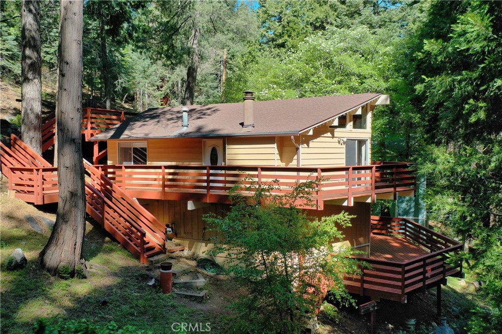 Experience the tranquil setting of “Dogwood Chalet”. Resting on a spacious 12,600 sq ft parcel with a soothing seasonal stream, this mountain retreat is nestled beneath soaring evergreen trees and surrounded by the most beautiful mature Dogwood trees. This well maintained cabin offers many amenities making it a front runner in its price range. With 1,416 sq ft, 3 bedroom/2 bathroom, this gem offers a special opportunity for families needing a private, separate entrance self contained guest quarters! Upon entrance of the upstairs you are greeted with a chalet style open beamed vaulted ceiling and double slider door wall of glass leading onto the upper deck. Luxury vinyl flooring throughout the entire upstairs with a cozy wood burning fireplace. 2 spacious bedrooms also with vaulted ceilings conveniently located on the entry level with full bathroom. A stackable washer/dryer in upstairs provides the ability for the upstairs and downstairs to be rented separately if desired. The lower level 3rd bedroom features its own entrance, newly installed luxury vinyl plank flooring(April 2025 install), full sized washer/dryer, and bathroom w/shower. A kitchenette area with fridge, two burner induction cooktop, sink, and spacious attached decking. This lower level can also serve as a spacious home office, home gym or game room. A great location provides easy access, conveniently located off a county paved and maintained road near Hwy 189 making it a breeze to head off the mountain. Level parking on a spacious parking deck completes the package. Truly a story book setting, Dogwood Chalet is ready for its next owners to rejuvenate body and mind amongst the beautiful pines of Twin Peaks!