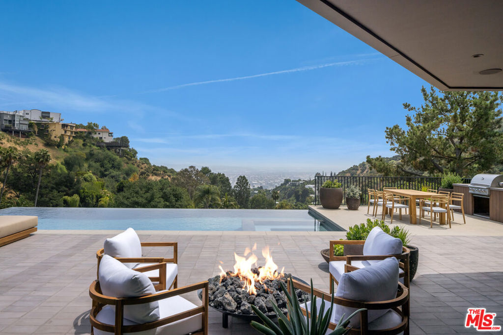 Floating high above the city on the Sunset Strip, this reimagined mid-century residence has been thoughtfully restored and expanded to reflect contemporary ease without compromising its storied soul. Past a gated entry, a peaceful zen garden introduces the home with intentionsoft landscaping and clean architectural lines that give way to interiors that feel both elevated and grounded. Terra cotta flooring imported from Spain spans the main living areas, anchoring soaring open spaces where light pours in through floor-to-ceiling sliders and wraparound windows framing unobstructed ocean and city views.A generous formal living room offers both drama and intimacy with warm plaster walls, a wood-burning fireplace, and a custom bar encased in artisan Oak cabinetry. A cozy theater room with concealed bespoke millwork doubles as an additional seating lounge overlooking the front gardens. The kitchen is a singular showpiece, fully customized in rich chocolate and oak tones with an integrated island, Gaggenau appliances, Vola brass fixtures, double fridge/freezer, with stunning Heath tile and Limestone counters with an integrated stone sink. The adjacent dining area opens completely to the poolside deck for seamless entertaining. Once outdoors, a negative-edge pool spills into the horizon, flanked by a volcanic rock fire pit, BBQ/ kitchen area with dining for ten, outdoor shower and bathroom, as well as an epic, wraparound terrace for breathtaking, panoramic sunsets. Adjacent to the formal living room, a conveniently separated family room with a floor-to-ceiling fireplace looks out onto the front courtyard and includes a full bathroom. This area leads to a private guest suite with a luxuriously appointed ensuite complete with soaking tub, shower, heated floors, along with a dedicated work nook, and two separate terraces. Thoughtfully framed for private entry, this wing has the flexibility to serve as an ADU and ideal guest retreat. A second guest bedroom enjoys a skylit foyer, large closet, balcony, and built-in vanity.Each bedroom is designed as a tranquil hideaway, all with private terraces and access to nature. The primary suite is wrapped in glass, oriented toward the horizon and offering sweeping views from bed to bath. Dual walk-in closets and dual bathrooms with radiant heated floors, steam showers, custom cabinetry, a marble soaking tub, integrated makeup vanity, and a refrigerated beauty drawerbring a level of detail rarely seen. A large office with its own walk in closet, ensuite and terrace can flex easily as an additional bedroom, while the gym with convenient small refrigerator opens to yet another private outdoor space. Other notable amenities include a double laundry room with utility sink, Control4 smart home system, and a two-car garage beyond a secured entry.With cinematic views and a soulfully executed interior, this Sunset Strip hideaway delivers a living experience that's as dynamic as its surroundings. Framing some of the most spectacular vistas in all of Los Angeles, this residence offers a front-row seat to sun-drenched days and electric city nights an immersive perspective few homes can rival.