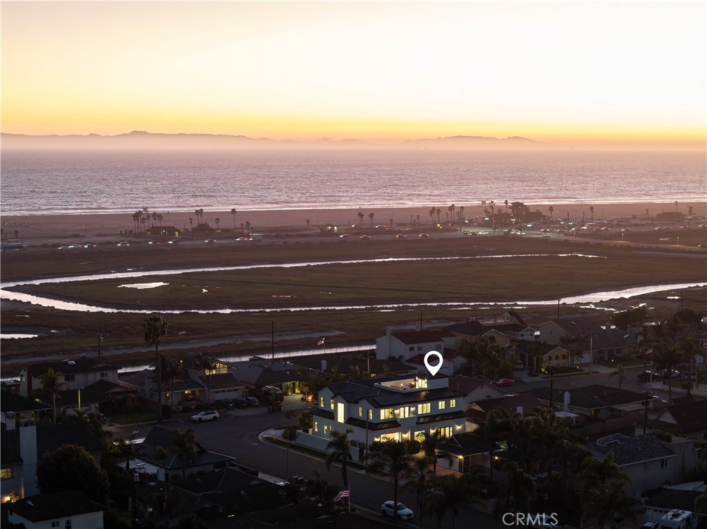 Completed in 2025, this brand-new coastal estate at 9121 Christine Drive sets a new standard for luxury in Huntington Beach. Positioned on a premier corner lot, the home offers nearly 5,000 sq. ft. of living space and a spectacular 560 sq. ft. rooftop deck with unobstructed ocean views. Designed with both form and function in mind, it combines timeless architectural detail with state-of-the-art construction and absolutely premium materials. Step inside to soaring 11-foot ceilings adorned with custom wood beams, wide-plank European white oak flooring, and natural light streaming through Milgard windows and French doors. Indoor and outdoor living flow seamlessly thanks to a dramatic La Cantina pocket door that opens to the main entertaining space, anchored by a Belvedere book-matched marble fireplace. The main kitchen showcases white oak cabinetry, Taj Mahal quartzite counters, a 72” Sub-Zero refrigerator, 48” Wolf range, and Sub-Zero wine fridge. A separate butler’s kitchen, with Thermador appliances and a walk-in pantry, ensures effortless hosting. The primary suite is a true retreat with vaulted ceilings, a stone fireplace, alabaster marble chandeliers, and a 30-foot balcony capturing ocean breezes. Its spa-inspired bath boasts full-slab marble shower walls, a custom double vanity with Brizo polished gold fixtures, and a boutique-style walk-in closet with illuminated white oak cabinetry. Additional highlights include a three-car garage with custom rift oak doors, an elevator servicing all levels, two laundry rooms, a solar system, and a durable metal roof. Designer guest baths feature Porcelanosa and Ann Sacks tile, while a Taj Mahal quartzite wet bar adds sophistication to the entertaining level. With no expense spared and every finish hand-selected, this one-of-a-kind residence blends architectural excellence with unmatched coastal living—moments from the sand and surf of Huntington Beach.