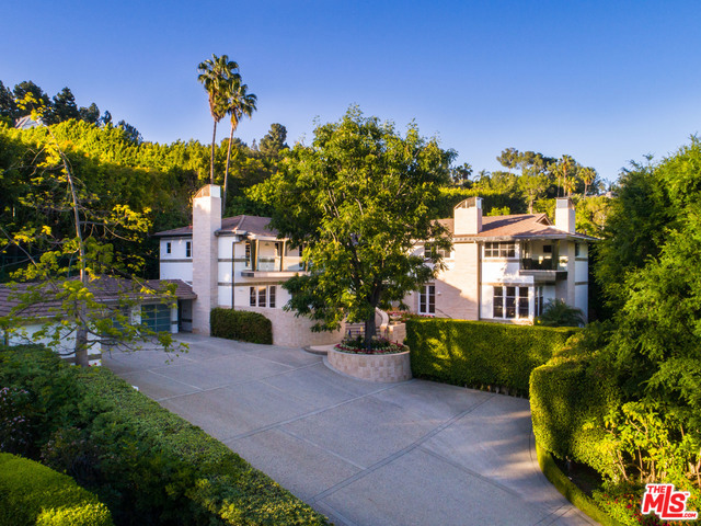 Tucked behind gates on over an acre of lush grounds, this exquisite modern estate with a rich Hollywood history claims a prized double lot in one of Beverly Hills' most coveted neighborhoods. Perched atop a hillside, the main residence features generous, light-filled living spaces, including an expansive family/media room with a bar, fireplace, and temperature-controlled wine room; chef's kitchen; sun room; formal dining room; staff quarters and an elevator. The second story holds a voluminous master suite with dual bathrooms and walk-in closets, an adjoining office and gym, and French doors to a private terrace, as well as two en-suite guest rooms. Primed for entertaining, the sprawling verdant grounds create an oasis that boasts a pool and spa with a bath, water and fire features, as well as a fully-hedged and lighted tennis court. A guest house, 3-car auto gallery, expansive motor court with parking for 25 cars and a security and Smart Home system complete this phenomenal estate.