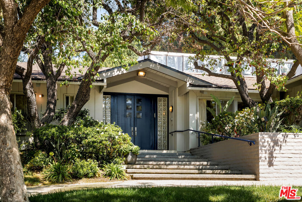 Set back from the street below towering Mexican fan palms, this California ranch-inspired home is a fusion of contemporary and midcentury influences on a mostly one-level floor plan in highly sought Beverly Hills proper. A circular driveway leads to carefully manicured landscaping and mature trees complementing the home's elegant and inviting double-door entry flanked by fashionable glass blocks. Inside, vaulted ceilings elevate the foyer and public entertaining spaces. In the family room, a magnificent mirrored fireplace reflects natural light as sliding glass opens to the rear grounds near a smartly designed wet bar for serving multiple party guests. The adjacent formal living room is perfect for intimate gatherings and quiet conversation. Upstairs, a partial loft-style bonus room is ideal as a media room, office, guest quarters, game room, and more, complete with a private balcony overlooking the backyard below. The striking kitchen is both a conversation piece and gourmet culinary center, outfitted with copious cabinetry, smooth glossy countertops, center island with cooktop and hood, hot plate, recipe desk, and premier brands such as Sub-Zero and Miele. Floor-to-ceiling windows in the adjacent eat-in area showcase views of the serenity that awaits outside, accessible via sliding glass door to maximize indoor-outdoor flow. The formal dining room, positioned off of the entry, is excellent for hosting family and friends on special occasions. A voluminous owner's suite has vaulted ceilings, picture windows, direct pool access, and an en-suite spa-like bath with dual vanities, makeup station, jetted tub, and separate shower. Secondary bedrooms are en-suite and light-filled. In the backyard, enjoy an abundance of patio space, lounging decks, built-in seating, outdoor living and dining areas, lush atrium/garden, and pool and spa with water feature, all enveloped by leafy greenery. This world-famous, sought-after location provides access to coveted City of Beverly Hills services such as schools, utilities, and police, just moments to the high fashion of Rodeo Drive, Century City, and the many offerings of the Westside.