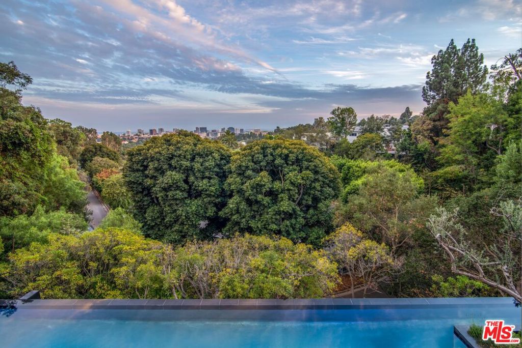 Masterfully nestled amongst lush, Mediterranean-style landscaping in Bel Air, this glass-encased home designed by renowned architect Paul McClean, defines California luxury living. Featuring deeply connected architectural design and finishes to the highest level, the home includes a 3-level waterfall feature that flows into a reflecting pool, floor-to-ceiling wood paneling, and expansive living spaces with soaring ceilings. The majestic use of limestone and oak adds softness to the estates contemporary aesthetic with seamless boundaries between indoors and outdoors. The immaculate pool and spa are surrounded by a McClean signature, step-stone, water courtyard with a double-sided fireplace lounge. Upstairs, a palatial primary suite overlooks far-reaching views of the city from a massive outdoor deck, breathtaking dual bathrooms, and a retail-style glass closet. Skylights beam light into 6 ensuite guest bedrooms, with downstairs gym, wellness area, 20-person theater, and temperature-controlled wine room.