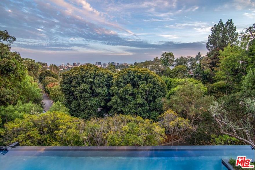 Masterfully nestled amongst lush, Mediterranean-style landscaping in Bel Air, this glass-encased home designed by renowned architect Paul McClean, defines California luxury living. Featuring deeply connected architectural design and finishes to the highest level, the home includes a 3-level waterfall feature that flows into a reflecting pool, floor-to-ceiling wood paneling, and expansive living spaces with soaring ceilings. The majestic use of limestone and oak adds softness to the estates contemporary aesthetic with seamless boundaries between indoors and outdoors. The immaculate pool and spa are surrounded by a McClean signature, step-stone, water courtyard with a double-sided fireplace lounge. Upstairs, a palatial primary suite overlooks far-reaching views of the city from a massive outdoor deck, breathtaking dual bathrooms, and a retail-style glass closet. Skylights beam light into 6 ensuite guest bedrooms, with downstairs gym, wellness area, 20-person theater, and temperature-controlled wine room.