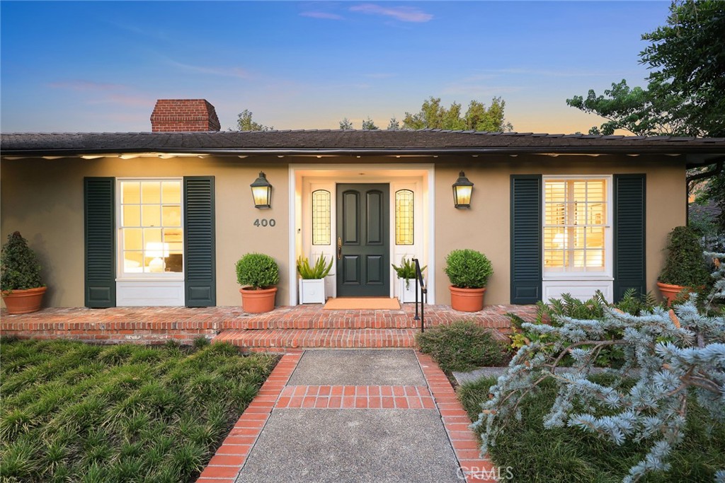 Located on one of the most desirable streets in the Lower Rancho neighborhood, directly behind the L.A. County Arboretum where majestic peacocks roam freely, this timeless ranch home offers the epitome of indoor/outdoor Southern California living.
Originally the personal residence of nationally-honored Landscape Architect Bob Eriksson, FASLA, the property showcases thoughtfully designed gardens and elegant living spaces. Set back from the street and framed by mature trees, the home features a charming brick front porch, large double-hung windows, and custom shutters.
Inside, the foyer with paneled door and leaded glass windows opens to a welcoming living room with fireplace, which flows seamlessly to the skylit formal dining room and expansive beamed family room. A wall of glass and arched French doors highlight garden views, extending to the breakfast room and kitchen. The kitchen and adjacent wet bar include custom cabinetry, stone counters, and garden vistas, with convenient access to the mud/laundry room.
The bedroom wing offers 3 bedrooms and 3 full baths (2 en-suite). The spacious primary suite features a tray ceiling, sitting area, wood-paneled closets, and French doors opening to the garden. The second en-suite bedroom enjoys its own private deck, perfect for morning coffee or quiet retreat.
The rear yard unfolds across two levels with brick patios, signature concrete steps, an 8-jet in-ground spa, hillside dining deck, and a curated collection of specimen trees including a grove of eight mature Redwoods, a producing Avocado, Japanese Maple, California Sycamore, Carrotwoods, and more.
Beautifully maintained and sensitively updated with a new tile roof, refinished hardwood floors, fresh paint, and new carpet, this move-in ready home is a rare offering in a coveted location—perfect for everyday living and gracious entertaining.
