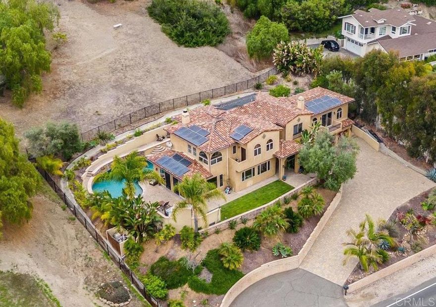 From the moment you arrive at this custom West Olivenhain estate—perched above the San Elijo River Valley—you’ll feel the presence and charm of a truly special home. The extended paver driveway and lush tropical landscaping lead you away from the hustle and bustle and into your own private coastal retreat. Spend your days floating in the saltwater pool, unwinding in the spa, or entertaining friends and family with seamless indoor/outdoor living. As evening falls, curl up beside the outdoor fireplace under glowing bistro lights and let every moment feel like a vacation at home.  Inside, natural light floods through wood-cased windows and soaring ceilings, showcasing custom craftsmanship at every turn. The front living room features stunning arched windows that frame the tropical landscape, while a reimagined fireplace clad in El Dorado White Elm stone creates the perfect spot to relax with conversation or a quiet cup of coffee. Continue through the formal dining area—also opening to the rear yard—and into the heart of the home: a spacious great room that flows effortlessly outdoors through multiple sets of doors, creating a true entertainer’s dream.  The remodeled kitchen anchors the space with stainless steel appliances, a gas range with statement hood, custom cabinetry, Opulence Quartz countertops, a walk-in pantry, and a cozy breakfast nook. The adjoining family room, complete with a second fireplace, overlooks the lush backyard oasis.  Step outside and be transported to your favorite tropical destination. The resort-style yard showcases a saltwater Pebble Tec pool and spa, custom stone fireplace, built-in BBQ island, terraced gardens, and paver walkways—all illuminated by upgraded solar-powered landscape lighting. With owned solar for both the home and pool, energy efficiency meets luxury.  Upstairs, the spacious primary suite feels like a private retreat with custom wood shutters, wood-cased windows, a balcony overlooking the preserve, an oversized walk-in closet, and a spa-inspired bath with dual sinks and a steam shower. Additional upstairs highlights include a junior suite, two secondary bedrooms with a shared bath, and a large fifth en-suite bedroom with a private entrance—ideal for a guest suite, ADU, office, or studio.  Additional features include a three-car garage with custom wood doors, epoxy flooring, and built-in cabinetry, as well as storage sheds, a tile roof, solid wood interior doors, 3-zone AC, surround sound, and more.  This is a rare opportunity to own a one-of-a-kind luxury estate in one of Encinitas’ most sought-after communities.