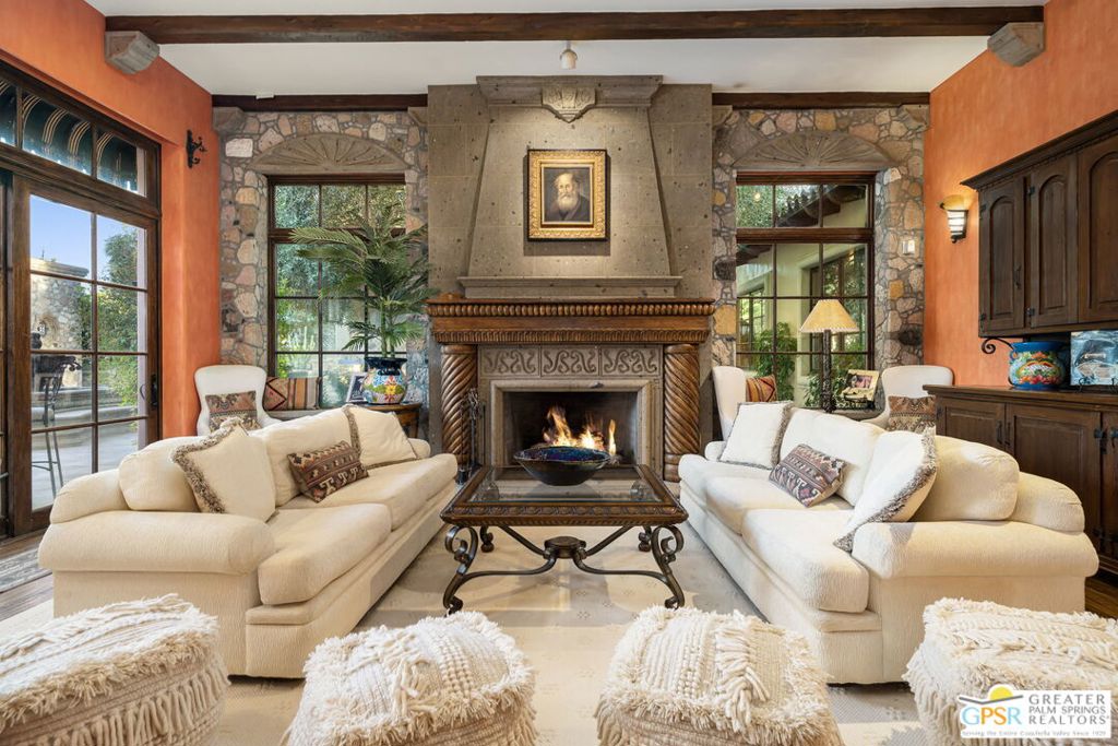 "La Belle Dame" is a masterpiece by Juan Carlos Ochoa in Clancy Lane Estates. In the heart of Rancho Mirage's most coveted enclave, this gated, one-acre Mediterranean-inspired estate by celebrated architect Juan Carlos Ochoa is a singular work of art, uniting Old-World craftsmanship with resort-caliber amenities. Restored inside and out, the 6,424 sq. ft. single-level villa offers an unparalleled blend of architectural integrity, privacy, and timeless luxury. Pass through custom wrought iron gates into a secluded world where mature cactus gardens, an olive tree grove, and mountain views set the tone for the extraordinary. At the center of a sweeping motor court, a 10-foot hand-carved Cantera stone fountain commands attention. Two separate garages, one attached that is climate controlled, one detached, offer parking for four, with additional guest parking for six. Every detail speaks to Ochoa's signature craftsmanship: Mexican Saltillo tile and hand-hewn oak plank floors, vaulted ceilings with exposed beams, arched passageways, bullnose corners, and hand-carved stone fireplaces. Custom Italian Albertini doors and cabinetry, Venetian plaster walls, intricate ironwork, and stone corbels are woven throughout the interiors, evoking the romance of a Spanish monastery while providing the comfort of modern living. The formal living room, anchored by a grand fireplace and wood-beamed ceilings flows seamlessly to the terrace through French doors. A spacious formal dining room leads to the chef's kitchen, crowned with a stained-glass illuminated ceiling, Wolf range, dual ovens, butler's pantry, Sub-Zero refrigeration, and a 200-bottle custom climate controlled wine cabinet. Multiple entertaining areas, both formal and casual, open to the outdoors, blurring the lines between interior elegance and exterior splendor. The primary wing is a sanctuary with dual walk-in closets, spa-inspired bath adorned with hand-painted Spanish tile, private den, and an executive office. Three additional ensuite bedrooms each offer distinctive character and luxurious finishes. A poolside cabana with half bath ensures guest comfort during long afternoons in the sun. The south-facing backyard mirrors a private resort, tiled swimming pool framed by gas fire bowls, spa in a stone grotto, four-sided stone firepit, and a pavilion with a fully equipped outdoor chef's kitchen. Multiple stone fountains, lush gardens, and intimate patios create a series of enchanting vignettes for entertaining or quiet reflection. Clancy Lane Estates is a gated, private sanctuary renowned for its exclusivity and proximity to world-class dining, shopping, golf, and cultural attractions. This home is more than a residence, it is a once-in-a-lifetime acquisition for the connoisseur of fine architecture and unmatched craftsmanship. This work of art is shown to qualified buyers by appointment only.