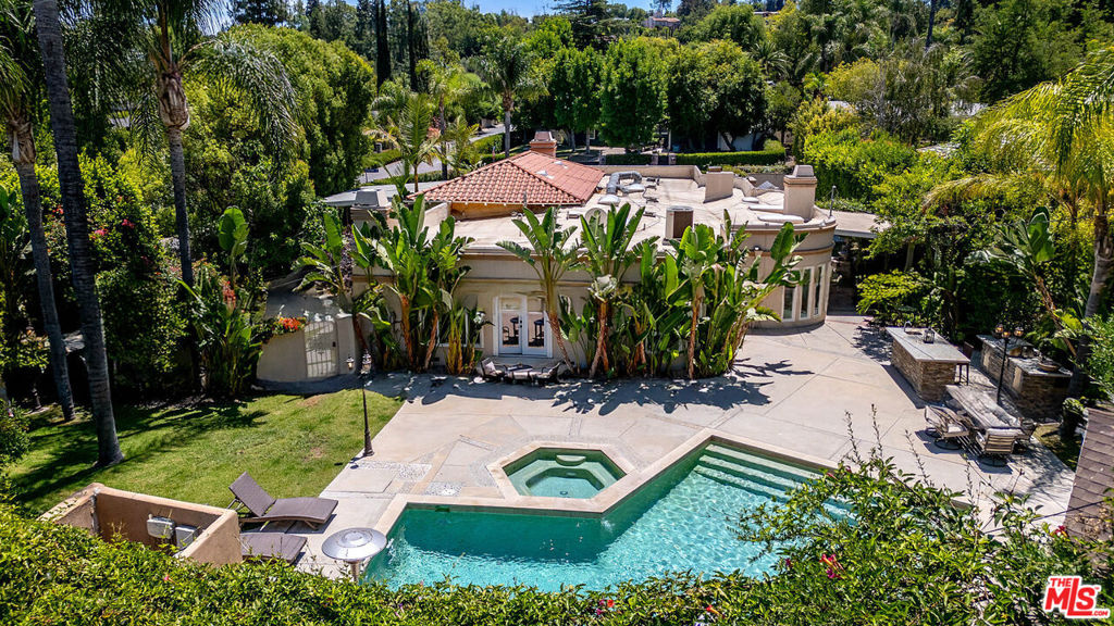 Welcome to this expansive and tastefully updated 5-bedroom, 3.5-bathroom home, nestled on a private, lushly landscaped lot in a prime Woodland Hills neighborhood. This elegant home boasts soaring ceilings, arched-top windows, and stunning curved bay windows that flood the space with natural light. This beautiful house has 3 fireplaces, 5 outdoor fire pits, 3 fountains with state-of-the-art alarm and camera system with remote access. Inside, you'll find a sophisticated blend of marble and wood flooring throughout, creating a warm yet refined ambiance. The formal living room with a fireplace and adjoining dining area are ideal for entertaining, while the oversized family room features a wet bar and enough space for a billiard table. The third bedroom, located just steps from Primary Bedroom 1, offers flexible use as a nursery, playroom, or guest room. The open-concept kitchen, recently remodeled with custom cabinetry and modern appliances, seamlessly connects to the family room and is perfect for hosting gatherings or everyday living. The first primary suite with fireplace opens directly to the backyard, offering a perfect blend of indoor-outdoor living. The second primary bedroom showcases curved bay windows for beautiful natural light throughout the day. Additional features include a dedicated home office with wall-to-wall bookshelves and en-suite bath, plus a garage which has been converted to den/conference room, with sleek cabinetry that can be used as a guest room. Step outside to your private outdoor oasis, where multiple seating areas, a raised fire pit with a cascading waterfall into the pool, fire bowls, a built-in BBQ, and a cozy gazebo with its own fireplace and sitting area offer year-round enjoyment. Stylish, spa-inspired bathrooms, generous living spaces, and meticulously designed outdoor areas make this home a rare gem. A truly special opportunity to own a luxurious and comfortable retreat in the heart of Woodland Hills.