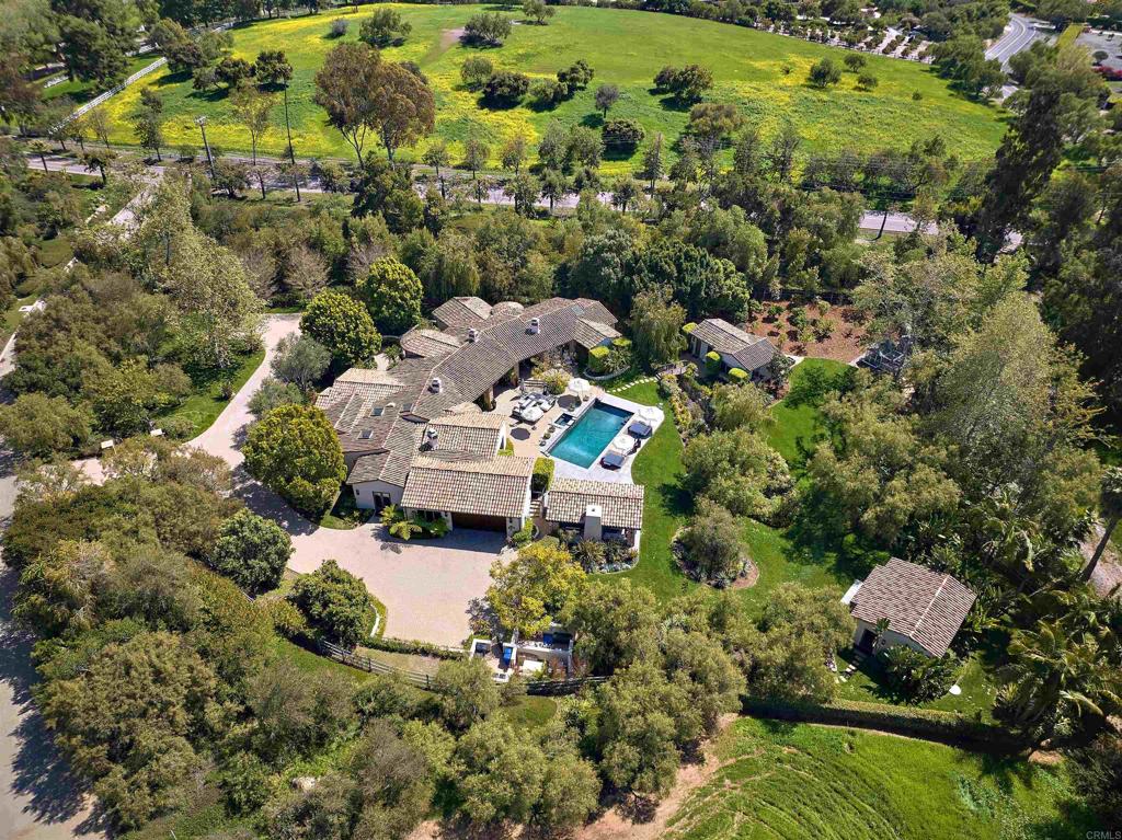 Set behind private gates on over three beautifully landscaped acres in the heart of the Rancho Santa Fe Covenant, 18320 Colina Fuerte is a rare, single-level estate offering effortless luxury, timeless design, and resort-style living. Perfectly positioned along the renowned RSF riding and walking trails, this recently reimagined residence captures the essence of Southern California living at its finest. Spanning nearly 8,000 square feet, the main residence has undergone a complete, high-style transformation. Every detail has been thoughtfully curated — from the all-new custom kitchen and spa-inspired baths to the dual primary closets and the exquisite designer lighting found throughout the home, including fixtures featured in Mr. & Mrs. Smith. Elevated finishes, new wood and porcelain tile flooring, and bespoke details enhance each space. The floorplan offers four en-suite bedrooms, a richly paneled executive office, a luxe theater room, and a versatile bonus room ideal for a playroom, gym, or studio. Two detached structures provide added flexibility: a fully self-contained 600-square-foot guest house perfect for multigenerational living or visiting guests, and a third building currently used as a gym—ideal as a detached office, creative studio, or additional guest quarters. Indoor-outdoor living is seamless and inspired. French doors lead to expansive resort-style grounds, complete with a sparkling pool and spa with cascading water features, an outdoor living and dining pavilion with built-in heaters and a firepit, and a full outdoor kitchen featuring a wood-fired pizza oven. A wide, grassy lawn offers space for play, while mature landscaping, fruit trees, and a charming chicken coop add whimsy and character. Car enthusiasts will appreciate the attached two-car garage outfitted with lifts, providing space for up to four vehicles. Additional enhancements include newly added stone exterior accents, a central vacuum system, dual-pane Andersen windows and doors, and a state-of-the-art X-Tech security system with cameras for ultimate peace of mind. Located in the prestigious Covenant of Rancho Santa Fe, residents enjoy exclusive access to the RSF Golf Club, tennis and pickleball courts, miles of private equestrian and walking trails, the charming Village with its shops and restaurants, and a top-rated K-8 public school — all just minutes from coastal attractions, freeways, and world-class amenities. Turnkey, private, and exquisitely updated, 18320 Colina Fuerte is a rare opportunity to own one of Rancho Santa Fe’s most compelling luxury estates.