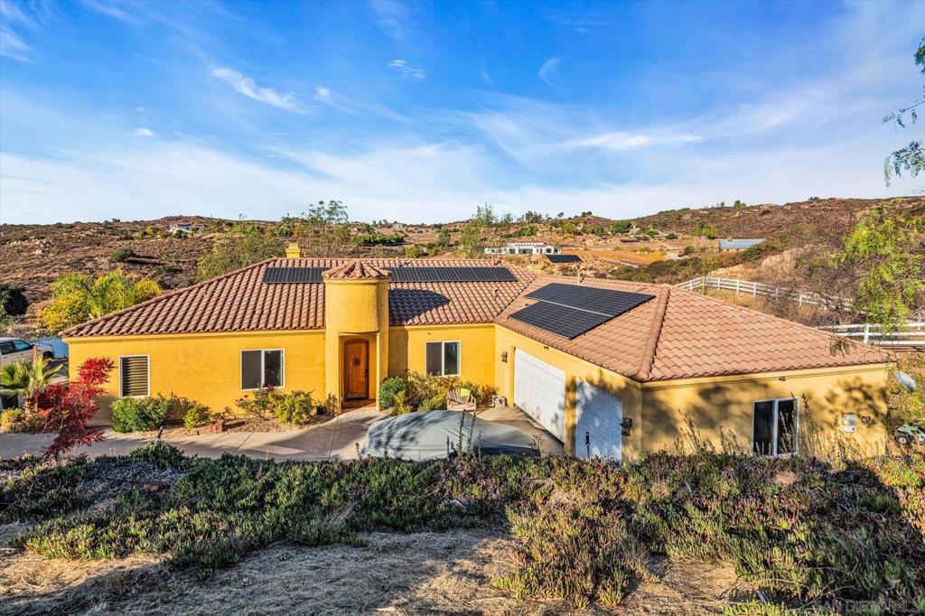 Stunning West End Ramona Retreat with Panoramic Views, Paid-Solar and Room to Grow! Serene sunrises and breathtaking sunsets await you at this exceptional 3.29-acre estate in Ramona’s highly desirable West End, just minutes from the region’s wine country. Built in 2005, this meticulously maintained 3,000 sq ft home offers a rare combination of privacy, elegance, and versatility—with no HOA, fully paid solar with Tesla battery backup, fast internet avail. and panoramic views of the surrounding hills and tranquil pond. Step inside to discover soaring, 10-foot-high ceilings, custom wood shutters, new Milgard windows, dual zone climate control, and 8-foot doors. Abundant natural light creates a welcoming, airy atmosphere. The gourmet kitchen is a chef’s dream, featuring granite countertops, built-in ovens, a large center island, and a drop-in gas range. Enjoy peaceful morning views from the breakfast nook and cozy evenings by the fire in the open concept living area. The private master suite is a true sanctuary with its own fireplace, walk-in closet, luxurious en-suite bathroom with dual stone vessel sinks, soaking tub, walk-in shower, and private outdoor entrance with serene pond views. On the opposite wing of the home, two generously sized bedrooms share a full bathroom, along with a conveniently located powder room. This thoughtfully designed home also offers multiple flexible living spaces, including a formal dining room, a spacious den or library with a third fireplace and stunning views, and an additional bonus room ideal for a home office, gym, or playroom. The large indoor laundry room includes a sink, counter space, and abundant storage. A three-car garage and expansive private driveway provide ample room for vehicles, RVs, or recreational toys. The outdoor spaces are just as impressive. The property includes a fully fenced backyard, ideal for a future pool or outdoor kitchen, as well as a three-rail vinyl-fenced area perfect for horses, animals, or agricultural use. With a sloping northern terrain, this property could potentially create the ideal climate conditions for a boutique vineyard—offering a chance to embrace the wine country lifestyle from the comfort of home. Additionally, a second-level pad to the west of the property offers further potential to build a guest house /ADU, shop, or use for additional parking including RV parking. This home features indoor and outdoor sprinklers, a durable tile roof, and a private well for ample water with no bill. With solar power, utility bills can be minimal or nonexistent, potentially saving you thousands of dollars per year which should help you in subsidizing the insurance costs. Wildlife sightings are common here, with wild birds, deer, and natural beauty on display year-round. At twilight, on the right night, the sky transforms into a breathtaking palette of colors, adding to the sense of peace and magic this home offers. This one-of-a-kind oasis invites you to relax, unwind, and enjoy the best of country living.