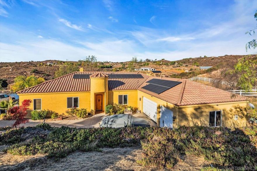 Stunning West End Ramona Retreat with Panoramic Views, Paid-Solar and Room to Grow!   Serene sunrises and breathtaking sunsets await you at this exceptional 3.29-acre estate in Ramona’s highly desirable West End, just minutes from the region’s wine country. Built in 2005, this meticulously maintained 3,000 sq ft home offers a rare combination of privacy, elegance, and versatility—with no HOA, fully paid solar with Tesla battery backup, fast internet avail. and panoramic views of the surrounding hills and tranquil pond.   Step inside to discover soaring, 10-foot-high ceilings, custom wood shutters, new Milgard windows, dual zone climate control, and 8-foot doors. Abundant natural light creates a welcoming, airy atmosphere. The gourmet kitchen is a chef’s dream, featuring granite countertops, built-in ovens, a large center island, and a drop-in gas range. Enjoy peaceful morning views from the breakfast nook and cozy evenings by the fire in the open concept living area.    The private master suite is a true sanctuary with its own fireplace, walk-in closet, luxurious en-suite bathroom with dual stone vessel sinks, soaking tub, walk-in shower, and private outdoor entrance with serene pond views.    On the opposite wing of the home, two generously sized bedrooms share a full bathroom, along with a conveniently located powder room.   This thoughtfully designed home also offers multiple flexible living spaces, including a formal dining room, a spacious den or library with a third fireplace and stunning views, and an additional bonus room ideal for a home office, gym, or playroom.  The large indoor laundry room includes a sink, counter space, and abundant storage. A three-car garage and expansive private driveway provide ample room for vehicles, RVs, or recreational toys.   The outdoor spaces are just as impressive. The property includes a fully fenced backyard, ideal for a future pool or outdoor kitchen, as well as a three-rail vinyl-fenced area perfect for horses, animals, or agricultural use. With a sloping northern terrain, this property could potentially create the ideal climate conditions for a boutique vineyard—offering a chance to embrace the wine country lifestyle from the comfort of home.    Additionally, a second-level pad to the west of the property offers further potential to build a guest house /ADU, shop, or use for additional parking including RV parking.   This home features indoor and outdoor sprinklers, a durable tile roof, and a private well for ample water with no bill. With solar power, utility bills can be minimal or nonexistent, potentially saving you thousands of dollars per year which should help you in subsidizing the insurance costs.    Wildlife sightings are common here, with wild birds, deer, and natural beauty on display year-round. At twilight, on the right night, the sky transforms into a breathtaking palette of colors, adding to the sense of peace and magic this home offers. This one-of-a-kind oasis invites you to relax, unwind, and enjoy the best of country living.