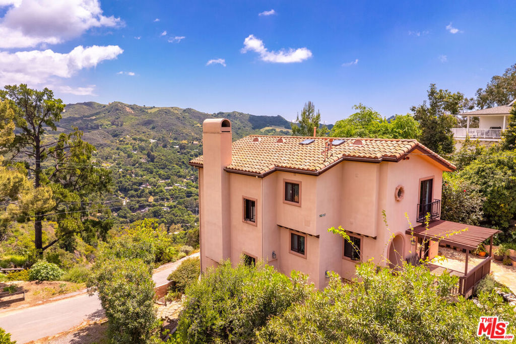 Perched high above the lush and serene hills of Topanga Canyon, this impeccable Mediterranean-style home welcomes you with a verdant native plants garden, its artisan-crafted front door and Saltillo-tiled foyer. The fireside living room bathed in natural light, features breathtaking, cross-canyon views of Topanga State Park and beyond. The gourmet kitchen is equipped with top-of-the-line amenities including a wine cooler, granite countertops, and a beautiful herb garden just outside. This home boasts hardwood flooring, open beam ceilings, handmade tiles and is complemented by spacious covered verandas and wrought iron details throughout. It includes 4 bedrooms and 4 baths, along with an office/5th bedroom on the lower level. The primary retreat features a cozy fireplace, French doors, soaring ceilings and a romantic covered balcony overlooking the mountains. Lush, manicured gardens feature koi ponds, waterfalls, sandstone boulders, a grassy area for play, and drought-resistant native plants. Additional amenities include an EV charger in the carport, a whole-house water filtration system and a laundry-to-landscape grey water system to conserve water. Safety features include built-in fire sprinklers. Enjoy the bounty of organic fruit trees, including Asian pear, apple, plum, lemon, and mandarin. Custom-built in 2001, this home is ideally situated mid canyon with easy access to both Malibu and The Valley.