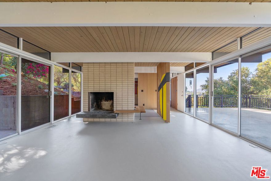 This Mid-Century post and beam home, originally designed by notable LA architect Dick E. Lowry AIA, is rare jewel tucked into the hills of Eagle Rock with stunning panoramic views. A striking profile set against a lush hillside backdrop, wrapped in warm wood siding and anchored by deep black trim, this beauty is bold from the start. Multiple decks spill out from the living spaces, creating a treehouse effect. Inside, walls of glass frame canyon and city views, while post-and-beam ceilings and wood paneling celebrate classic Mid-Century character. Recently redesigned by Yeh Design Lab with reverence for its architectural pedigree, the thoughtful updates imbue the home with a colorful and textural palette. From the brick fireplace surround to the minimalistic cabinet pulls in the kitchen, each element comes together in service of the original architecture. The kitchen is a vibrant mix of custom cabinetry, modern appliances and bold red & blue tile work that transform the space into a work of art. The bedrooms are spacious yet serene, warmed by natural wood and accented with clerestory windows that draw in the light. The bathrooms embrace a spa-like simplicity, including a dramatic outdoor shower framed by wood privacy enclosure. Sited on 3 lots, the home delivers multiple levels of outdoor spaces for entertaining, dining or soaking in the surrounding nature. The separate studio with far-reaching vistas, makes for a great home office, plus ample parking with room for 2 cars out front and 3 additional spots on the lot below. Just minutes from Eagle Rock's vibrant hotspots, this home has it all: prime location, architectural significance and connection to nature.