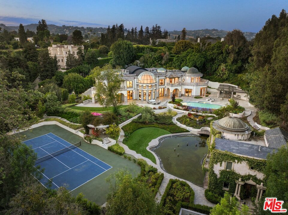 This stunning, incomparable Holmby Hills estate pairs grand, Old World European-inspired design with boundless modern amenities, palatial interiors, and 1.5 acres of gorgeous, park-like grounds. Surrounded by mature, leafy landscaping and a set behind a privacy-enhancing gate, 10350 Wyton Drive presents the pinnacle of divine, refined living. This three-level retreat encompasses six beds (all ensuite) and twelve total baths. Upon arrival, the main home presents a breathtaking two-story foyer with a double winding staircase, soaring cathedral ceilings, glass atrium, and floor-to-ceiling windows that invite in daylong natural light. Interiors encompass polished stone and hardwood floors, a chef's kitchen with Gaggenau appliances, an eight-seat theater, and elegant spaces to entertain. All bedrooms are on the second level, including the private primary suite. Outside, the lush, manicured grounds offer a pool, Jacuzzi, a pond, a tennis court, a gym, and enchanting gardens made for meandering. Additional features include a 13-car underground garage, 2 staff rooms, and a two-story four-bedroom, three-bath 2,900-square-foot guest house, which can host long-term visitors in total privacy and comfort. A true architectural masterpiece steeped in palace-like elegance, 10350 Wyton Drive is located in one of West L.A.'s most prestigious neighborhoods, mere minutes from museums, parks, the Los Angeles Country Club, and the shops and restaurants of Westwood and Beverly Hills.