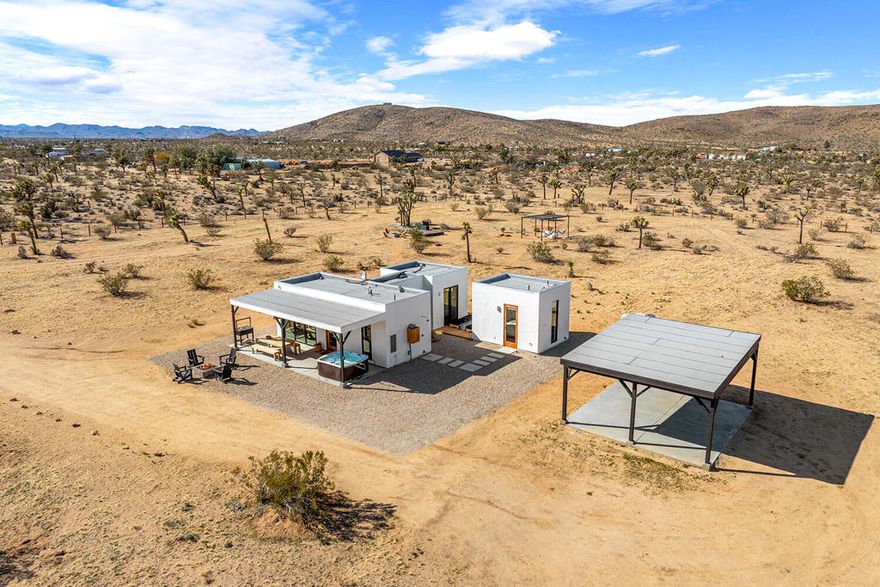 Tucked away on 4.5 private, fenced acres dotted with majestic Joshua trees, Sunny Sands is a modern architectural oasis designed for the ultimate desert escape. As you wind down the long driveway, the sleek, minimalist home emerges--a tranquil retreat bathed in golden sunlight and offering a seamless blend of luxury and nature. With panoramic mountain views, high-end finishes, and thoughtfully curated amenities, this one-of-a-kind property invites you to unwind, recharge, and soak in the beauty of the high desert.This unique retreat features three distinct structures, each offering its own charm and purpose. The primary residence is a modern, light-filled space with an accordion-style glass door that creates a seamless indoor-outdoor flow. A glass hallway leads to the serene bedroom, while the spa-like bathroom features handcrafted tiles and high-end finishes. The fully equipped kitchen and dry bar, stocked with Nespresso coffee, organic teas, and matcha, ensure that every moment is steeped in comfort. Across the teak deck, the casita provides a private escape with its own bedroom and half bath--perfect for guests or a quiet retreat. Adding a touch of rustic charm, the original homestead cabin stands as a nod to the property's past, offering an opportunity for transformation into a lounge, creative studio, or additional entertainment space.Indulge in luxury while embracing the simplicity of desert living. Spend your afternoons soaking in the private hot tub, cooling off in the recessed cowboy tub, or rinsing off in one of two outdoor showers as the desert breeze swirls around you. Enjoy panoramic views from various seating areas, test your swing at the golf practice net, or prepare an alfresco meal on the custom desert BBQ grill beneath the lighted pergola. As the sun sets, gather around one of the two firepits to watch the desert sky transform into a breathtaking canvas of stars.Perfectly blending modern design with the rugged beauty of the high desert, Sunny Sands is a rare find--a peaceful sanctuary just minutes from town and Joshua Tree National Park. Whether you're seeking a romantic getaway, a gathering with friends, or simply a place to disconnect and recharge, this breathtaking desert retreat promises an unforgettable experience.