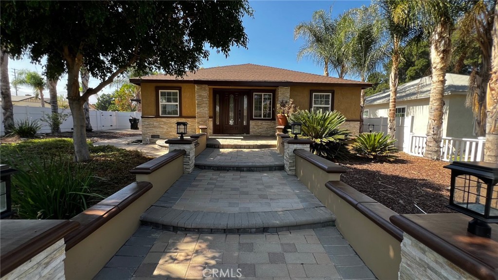 This is a warm real estate rental listing with a 4-bedroom, 2-bathroom home that highlights its key features: in-home laundry, a recently remodeled bathroom, abundant natural light, and a spacious kitchen island with a burner perfect for hosting family gatherings. It also has a white picked fence with large palm trees surrounding the home.