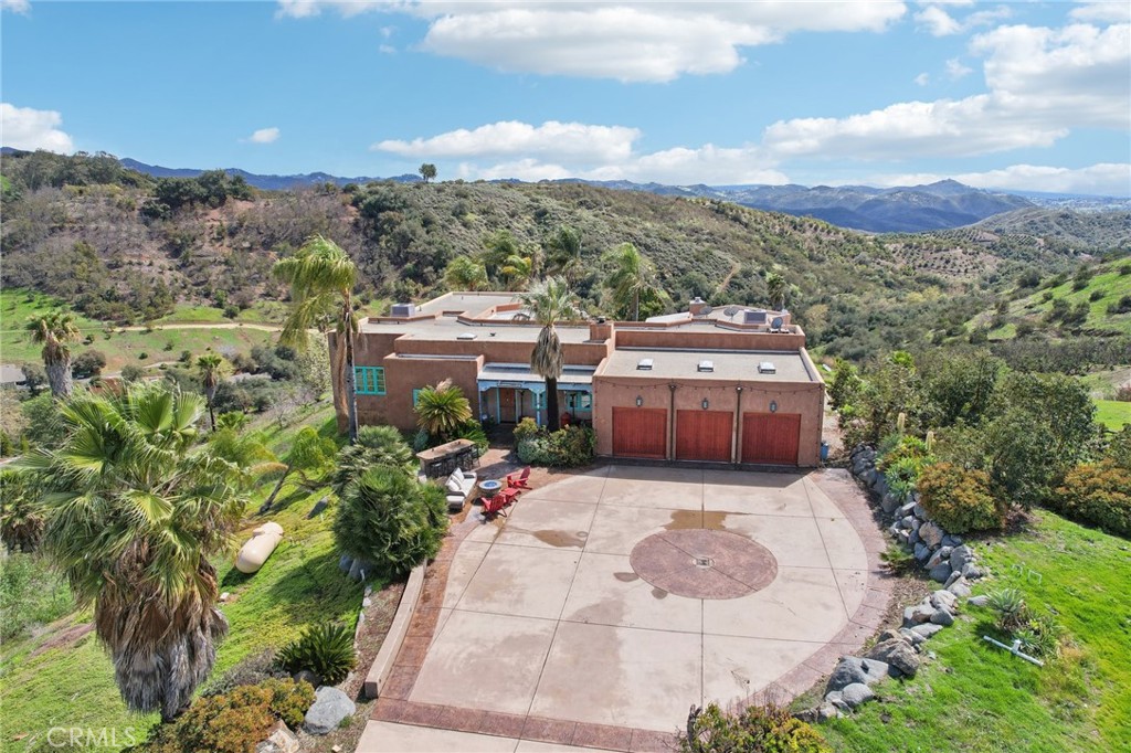 Adobe-Inspired Luxury Estate with Breathtaking Views in De Luz. Experience unmatched privacy, timeless style, and panoramic beauty in this one-of-a-kind custom adobe-style estate, nestled on over 4 acres in the prestigious hills of De Luz. From the moment you ascend the paved private driveway, you’ll be captivated by sweeping views and serene surroundings that instantly set the tone for this truly exceptional home. Designed with a distinctive Southwestern flair, every inch of this residence exudes character and craftsmanship—from the rounded fireplace in the living room to the custom wood doors with iron accents throughout. The heart of the home is the gourmet kitchen, where Wolf appliances, a Jenn-Air beverage fridge, and a custom-built island with breakfast bar create the ultimate culinary space. Expansive sliding glass doors blur the line between indoor comfort and the great outdoors, creating a seamless connection to the stunning natural landscape. Whether entertaining guests or enjoying a peaceful evening, the generous dining area and spacious living room offer both warmth and elegance. The layout is thoughtfully designed with four spacious bedrooms, including two luxurious suites. The primary suite, located in its own private wing, is a serene sanctuary featuring a fireplace, spa-like bath, and gorgeous views. A secondary suite also includes a fireplace and en-suite bath, while two additional bedrooms share a beautifully updated bathroom—ideal for family or guests. Convenience abounds with an indoor laundry room, complete with sink & cabinetry, & a second laundry area in the oversized three-car garage. The expansive driveway provides ample space for visitors, making entertaining a breeze. Step into your resort-style backyard, where every moment is framed by tranquility and jaw-dropping scenery. Lounge beside the sparkling pool and spa, sip wine at sunset on your private viewing deck, or relax in one of the many sitting areas thoughtfully placed throughout the grounds. With agricultural zoning, the opportunities here are endless—cultivate your own vineyard, orchard, or simply enjoy the space and seclusion. Just minutes from Old Town Temecula, award-winning wineries, fine dining, and with easy access to the 15 Freeway, this home delivers the perfect blend of peaceful rural living and urban convenience. Don't miss this rare opportunity to own a piece of paradise in one of Southern California's most coveted communities. Schedule your private tour today!