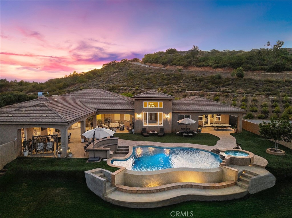 Welcome to 38150 Vía Huerta, a private, resort-style retreat nestled in the sought-after La Cresta community of Murrieta. Situated on 5 pristine acres with panoramic views of the mountains and city lights, this exceptional horse property offers the perfect blend of luxury, comfort, and functionality. From the moment you arrive, a gated entry and long, scenic driveway set the tone for the peaceful elegance that awaits. Inside, the home is filled with natural light and soaring ceilings that create a spacious, airy feel. Large picture windows frame breathtaking views and invite the outdoors in, while thoughtfully designed living spaces provide the ideal setting for both relaxation and entertaining. Inside, the oversized primary suite is a sanctuary of its own, complete with French doors opening directly to the pool and spa, and a spa-like bathroom with travertine finishes and dual vanities. A dedicated office and spacious guest bedrooms make this home as practical as it is beautiful. Step outside and you’ll find a true backyard oasis—an infinity-edge pool with waterfall features, a private spa, and a built-in BBQ area that’s perfect for gathering with family and friends. The covered patio and porch offer year-round comfort and are ideal for enjoying golden hour views over the valley. Equestrians will appreciate the 4-stall mare motel, corral, and miles of nearby horse trails. The property also includes a chicken coop, greenhouse, and an additional pad ready for fruit trees, a barn, or even a guest house. With 7 garage spaces, there’s no shortage of room for toys, tools, or a car collection. Whether you’re an entertainer, a hobby farmer, a horse lover, or simply looking for space to breathe, this one-of-a-kind estate offers it all.