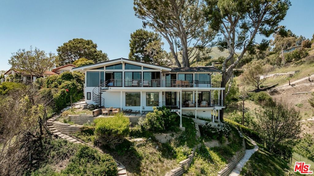 Nestled in the heart of Malibu, this architectural post-and-beam residence offers sweeping, unobstructed views of the ocean, city lights, mountains, and nearby islands. Positioned on a quiet cul-de-sac in the highly sought-after Malibu Knolls, this gated retreat exudes style, serenity, and natural elegance. Thoughtfully designed with floor-to-ceiling glass and rich wood beams throughout, the home seamlessly integrates indoor and outdoor living. The main level welcomes you with expansive living spaces, including a sunlit family room anchored by a wood-burning fireplace, a gourmet chef's kitchen with walk-in pantry, and an inviting dining areaall opening to wrap-around decks that frame the breathtaking views.This level also features three en-suite bedrooms, including a spacious junior primary suite, offering comfort and flexibility for guests or family members. The lower level is dedicated to the exceptional primary suite, a private sanctuary featuring a luxurious spa-like bath with oversized steam shower, soaking tub, generous walk-in closet, and direct access to private wrap-around terraces. Adding to the property's appeal is a detached guesthouse with its own entrance, private deck, and stunning ocean vistasperfect for visitors or creative workspaces. The terraced garden below offers room for play, reflection, or personal cultivation, while mature trees surround the property, providing rare privacy without sacrificing natural light or panoramic scenery.A true Malibu escape that effortlessly blends refined architecture with California's coastal beauty.