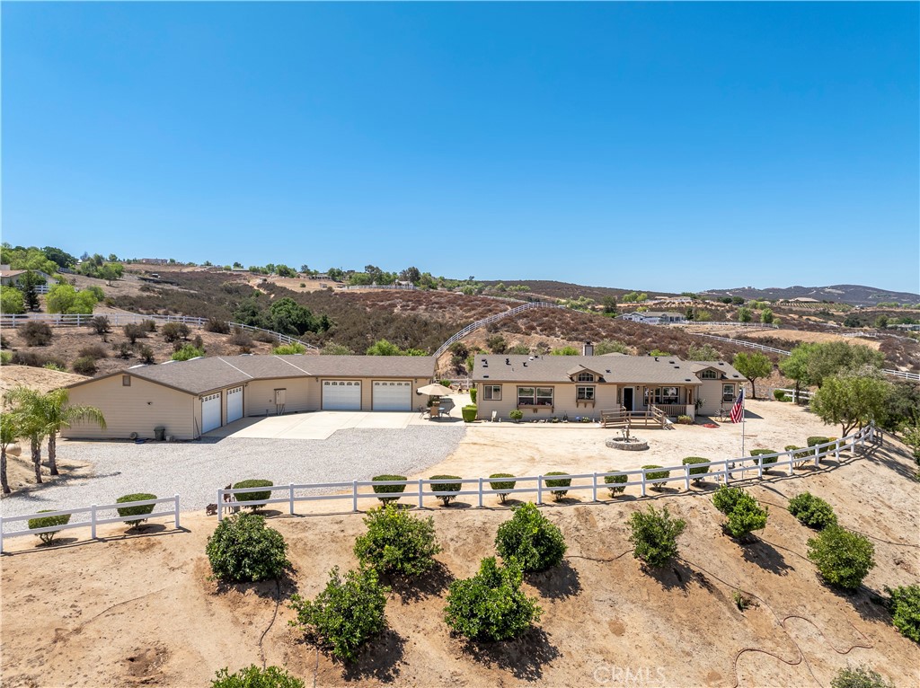 Welcome to 39597 Calle Escalona—an exceptional and meticulously maintained horse property located in the highly desirable Spanish Hills Rancheros community of Temecula Wine Country. Nestled on a rare, fully fenced 5.10-acre parcel, this one-of-a-kind estate offers breathtaking panoramic views of the Temecula Valley, unmatched privacy, and endless possibilities—all while being just minutes from city conveniences, top-rated schools, and renowned wineries. This spacious 4-bedroom, 2-bathroom manufactured home offers over 2,400 sq. ft. of comfortable, light-filled living space. The inviting floor plan features a cozy fireplace in the living room, generous common areas, and a large primary suite complete with a bonus retreat area, perfect for a home office, sitting room, or nursery. Outside, the property is loaded with premium features designed for both functionality and lifestyle. A detached 4-car garage houses a professionally built workshop equipped with multiple electrical outlets, 220V power, and an exterior RV plug—ideal for anyone needing serious workspace. You'll also find a dedicated RV clean-out on-site for added convenience. Enjoy the security and ease of the gated electronic entry, and the rare benefit of a fully fenced lot—a standout feature in this community. The property includes a private (non-shared) well, paired with a 7,500-gallon water storage tank, offering long-term peace of mind. A variety of mature fruit trees on a drip irrigation system enhance the outdoor space with seasonal beauty and productivity. There’s also plenty of usable land and room to add an ADU, barn, arena, or even plant your own private vineyard—the potential is limitless. Whether you're looking for a turnkey equestrian setup, a peaceful rural retreat, or an investment opportunity in Temecula’s Wine Country, this home delivers. With low HOA dues, incredible views, and country living just minutes from town, 39597 Calle Escalona is a rare opportunity you won’t want to miss.
