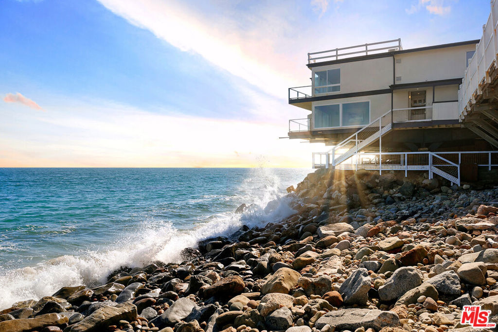A Coastal Sanctuary with Unmatched Views. Extraordinary end cap residence perfectly positioned on Big Rock Beach, just minutes from Santa Monica and central Malibu. This rare offering features two bedrooms plus a loft, and 2.5 bathrooms that are thoughtfully designed to showcase unobstructed, panoramic views of the ocean, Catalina Island, and the shimmering Queen's Necklace.Step inside to discover a warm and inviting interior curated for both relaxed living and elegant entertaining. The well-appointed kitchen and open dining area seamlessly flow into a sunlit living room with a balcony perched directly above the sea, offering front-row seats to stunning sunsets and the rhythmic sound of the waves.Upstairs, the romantic primary suite is a serene retreat, complete with an oceanfront balcony and an en-suite bathroom. A spacious open loft/family room area leads to the guest suite with a private bath, providing comfort and privacy for family or visitors. Step outside and indulge in the multiple outdoor living spaces, including an ocean-facing deck and a private subterranean patio perfect for al fresco dining by the crashing surf. With just a few steps, enjoy easy access to a picturesque cove and sandy pocket beach, an idyllic escape for sunbathing, swimming, or peaceful strolls along the shore. Additional features include an attached 1-car garage and carport for parking, and the quiet prestige of Malibu's storied Big Rock community. Combining modern amenities with the timeless soul of coastal living, this is beachfront living at its finest. This property has a strong history of short-term rentals and can be purchased with current furnishings for a seamless rental investment opportunity. 43 YEARS REMAIN ON LAND LEASE.