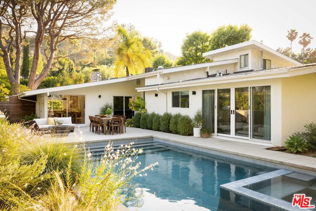 Tucked into a cul-de-sac in the quiet of Nichols Canyon Colony, this tranquil Mid-Century oasis seamlessly blends modern design with laid-back Hollywood Hills style. Past the entry, this beautifully reimagined single-story ranch offers 4 bedrooms, 3 baths, and an office, with views to greenery and the outside through every window. The home unfolds with ease: an open-concept kitchen anchors the home, flowing naturally into the family room, where vaulted ceilings, skylights, and a wall of glass draw the lush canyon setting inside. Mature landscaping frames the new pool and backyard designed by Johnston Vidal Projects, creating an idyllic outdoor sanctuary, with a built-in outdoor kitchen, gas firepit, and expansive grassy space. The formal living room, open to the dining room, is anchored by a floor-to-ceiling fireplace and verdant views to the front yard. An ensuite primary with two walk-in closets, a sumptuous soaking tub, and direct access to the pool, 3 bedrooms, 2 baths, an office, and a direct-access 2-car garage complete the home: a true refuge in the heart of Nichols Canyon.