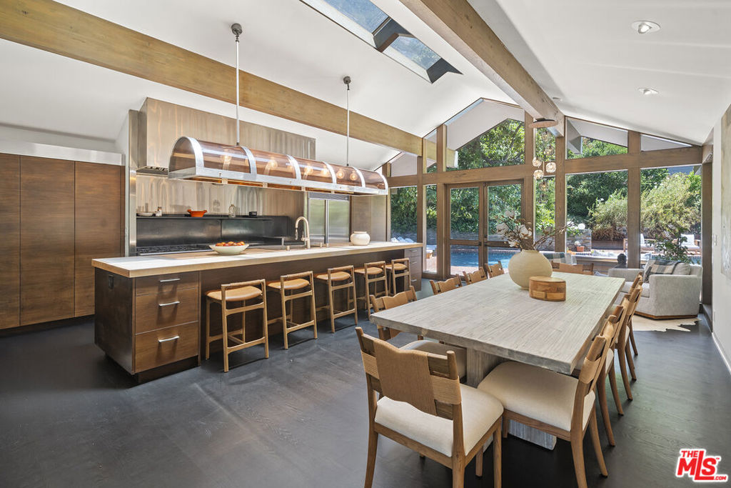 Where Timeless Character Meets Rustic Canyon Magic...Tucked away in the coveted Uplifters Ranch enclave of Rustic Canyon, this enchanting single-level retreat blends historic charm with modern sophistication just moments from the beach, Santa Monica, and Pacific Palisades. Originally built in 1924, it remains one of the last homes in the area to showcase a classic log cabin-style exterior oozing warmth, soul, and storybook appeal.Inside, natural light pours through skylights and floor-to-ceiling windows, highlighting soaring ceilings, wide-open spaces, and thoughtful design. A dramatic double-sided river rock fireplace anchors the semi-open layout, seamlessly connecting the formal living and dining areas with a stunning chef's kitchen and a peaked-roof family room overlooking the lush backyard and sparkling pool. The kitchen is a true standout, equipped with a professional-grade six-burner stove, double ovens, a griddle, and a lava rock gas grill. A large dine-in island and striking custom lighting complete the space, making it the heart of the home for cooking and gathering alike.The private primary suite is a serene sanctuary tucked away from the other bedrooms, featuring a newly reimagined spa-like bath with a marble walk-in shower, double-sized freestanding tub, twin vanities, and multiple skylights that bathe the space in natural light. Two additional bedrooms offer peaceful garden views, with one opening to the backyard through French doors. A cozy library with its own powder room, and an additional office or optional bonus room, provide flexibility for work, rest, or retreat.Outside, the verdant grounds are framed by mature trees, native landscaping, a grassy lawn, and even a fruiting avocado tree ideal for canyon living with a coastal breeze. This is a rare, once-in-a-generation opportunity to own a truly one-of-a-kind home in a magical, hidden pocket of Los Angeles where rustic elegance and relaxed luxury live in perfect harmony.