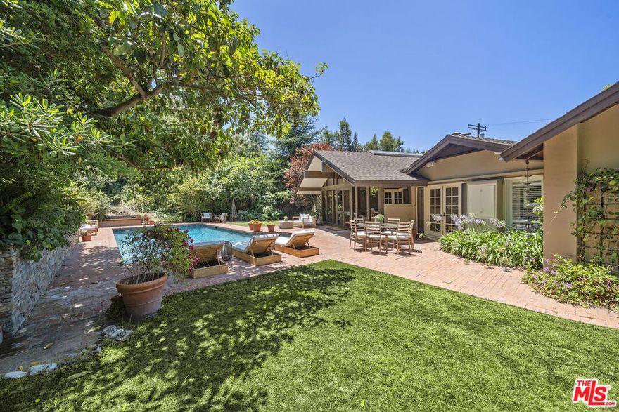 Positively idyllic, this one-of-a-kind Rustic Canyon Santa Monica residence blends historic charm with modern sophistication just moments from Will Rogers beach. Step inside and you're greeted by soaring ceilings, wide-open spaces, and natural light pouring in from skylights and floor-to-ceiling windows. A dramatic double-sided river rock fireplace anchors the semi-open layout, seamlessly connecting the formal living and dining areas. The kitchen is a true standout, featuring a professional-grade six-burner stove, double ovens, a griddle, and a lava rock gas grill, all centered around a large dine-in island with striking custom lighting. The private primary suite serves as a serene sanctuary, tucked away from the other bedrooms, with a newly reimagined spa-like bath showcasing a marble walk-in shower, a freestanding double-sized tub, twin vanities, and multiple skylights bathing the space in natural light. Two additional bedrooms offer peaceful garden views, one opening to the backyard through French doors. A cozy library with its own powder room and an office provide flexibility for work, rest, or retreat. Outside, the lush backyard and sparkling pool are framed by mature fig, avocado and redwood trees, native landscaping and a grassy lawn, creating a truly magical setting. Oozing warmth, soul, and storybook appeal, the home's rustic log exterior - originally sourced from early Hollywood movie sets - pays homage to the neighborhood's rich history as part of the storied "Uplifter's Ranch." The 17sf flat lot offers street-to-street access across from Rustic Canyon Park, complete with tennis courts, a nursery school and a community center for family-friendly activities. Travel further north on Latimer and the neighborhood culminates in a charming cul-de-sac with a bridge and creek. This unique, historic property embodies rustic elegance and relaxed luxury in one of the most enchanting, hidden pockets of Los Angeles. This home is more than a residence, it's a lifestyle.