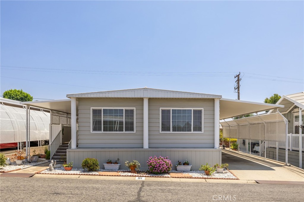 Meticulously Remodeled Home in Prime Location – The Casitas Mobile Home Estates (55+). Situated directly across from the clubhouse in the highly desirable Casitas Mobile Home Estates, this beautifully maintained and tastefully remodeled home offers comfort, style, and unmatched convenience in a senior community. Enjoy manicured grounds, a clubhouse, pool, and spa—all just steps from your front door. Charming curb appeal welcomes you with white rock landscaping and potted plants leading to an elevated, covered front deck with a privacy fence. Step inside to a spacious living room featuring large panoramic windows, abundant natural light, and warm laminate wood flooring. The adjacent formal dining area showcases arched openings and elegant built-in cabinetry. The remodeled kitchen complete with rich wood cabinetry, granite countertops, a peninsula perfect for casual dining or entertaining, and tile flooring that continues into the inviting family room. The family room also features a ceiling fan and sliding glass door access to the front porch. The primary bedroom is well-sized and offers plush carpet, a mirrored closet, and an en-suite bathroom with dual sinks, a vanity area, and a walk-in shower. The secondary bedroom also features carpeted floors, ample closet space, and direct access to the full hall bath—perfect for guests. Additional highlights include an indoor laundry area with cabinetry, a covered carport with a wheelchair lift for step-free access, and a convenient storage shed. The backyard offers a low-maintenance block planter and privacy wall for serene outdoor living.