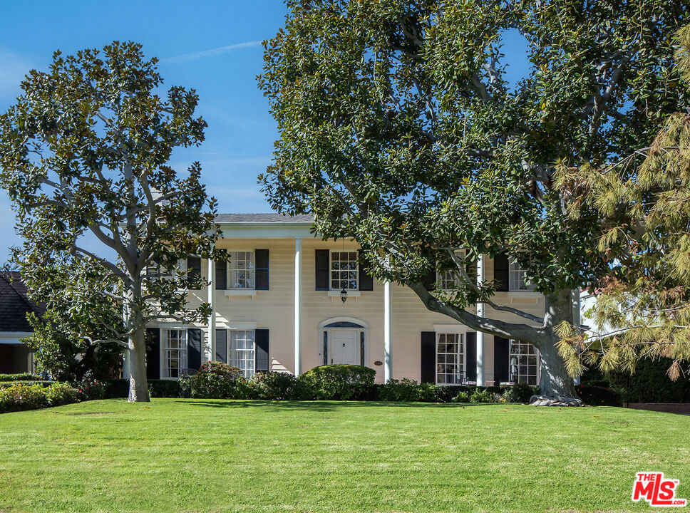 Tucked behind towering Southern Magnolia trees, this exquisite 5-bedroom, 5.5-bathroom estate embodies a seamless blend of classic elegance and contemporary comfort. A grand double-height foyer welcomes you into the voluminous residence, bathed in natural light throughout with expansive picture windows and glass doors. The formal living room is framed with charming French doors and extends onto the lush outdoor oasis, epitomizing indoor-outdoor, quintessential Beverly Hills living. Adjacent to the living room, a sunlit library office with bay windows and custom-built shelving, offers a tranquil retreat overlooking the picturesque patio and backyard. A beautifully updated chef's caliber kitchen features a waterfall porcelain island, top-tier appliances, cozy sitting lounge, and dining area, ideal for culinary endeavors and intimate gatherings. A spacious dining room overlooks the lush gardens with nearby powder room, and a convenient side entry leads directly into a thoughtfully designed laundry area and staff room, complete with a full bathroom. Upstairs, a sunlit landing with a sitting nook provides views over the manicured front lawn. The primary suite is a sanctuary of luxury with its own private balcony, a spacious sitting lounge, and dual-vanity bathroom featuring a soaking tub and shower. Closet space is plentiful throughout. The secondary primary suite also boasts a private balcony and ensuite bathroom with a tub and shower, overlooking the front and back gardens. Additional highlights include a large downstairs basement for ample storage. The outdoor spaces are equally captivating, featuring a large pool and spa, a BBQ and dining area perfect for alfresco entertaining, and a gated garage with an extended driveway. An outdoor bathroom ensures convenience for guests enjoying the poolside ambiance. This home blends sophistication and charm with thoughtfully designed spaces indoors and out, creating a true oasis for refined living. Capturing the essence of Beverly Hills living, this residence provides easy access to premier shopping, dining, and top-tier schools, as well as the city's exceptional services.