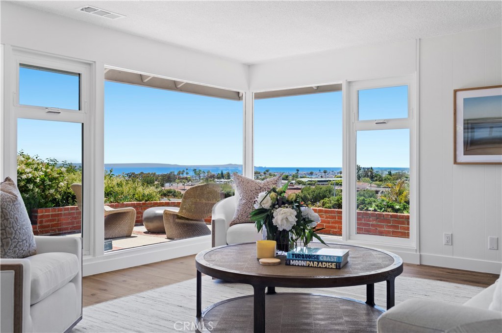 From the sparkling Pacific Ocean and romantic sunsets to dazzling city lights and Catalina Island, panoramic views enhance nearly every room of this impeccably maintained and carefully updated home in Corona del Mar’s sought-after Harbor View Hills. Walls of floor-to-ceiling windows wrap the single-level residence in glass, bringing abundant natural light indoors and welcoming vistas overlooking Fashion Island’s office towers, adjoining neighborhoods and Newport Harbor. The three-bedroom, two-bath design is approximately 2,474 square feet of free-flowing space. Offering magnificent ocean and city views, the living room opens to an intimate rear patio and features a classic brick fireplace, while the dining room offers access to the front yard and an ocean-view kitchen. White cabinetry and white countertops are complemented by a built-in pantry and upgraded stainless steel appliances, creating a functional and aesthetically pleasing space for mealtime preparation and entertaining. Both secondary bedrooms showcase ocean and evening-light views, and a generously sized family room displays a high ceiling with skylight, built-in cabinets and desks, and an adjacent laundry room with sink and ample storage cabinetry and shelving. Mid-Century style characterizes the large primary suite, which opens to the front patio and presents an interior French door to the family room, extensive mirrored closets, a period-perfect sunken tub, elegant floating vanity, and a shower with custom frameless-glass enclosure. Renovated in 2024, updates include a kitchen pass-through, Dutch door, refreshed landscaping, and upgraded showers with newer frameless doors. Additional improvements include new interior paint, new lighting, and a new epoxy floor in the two-car garage. Grounds measure nearly 7,128 square feet, allowing room for a circular driveway and an exceptionally private walled front yard with raised patio and low-maintenance turf. Harbor View Hills is directly across the street from Corona del Mar Plaza, beaches, and award-winning schools are minutes away.