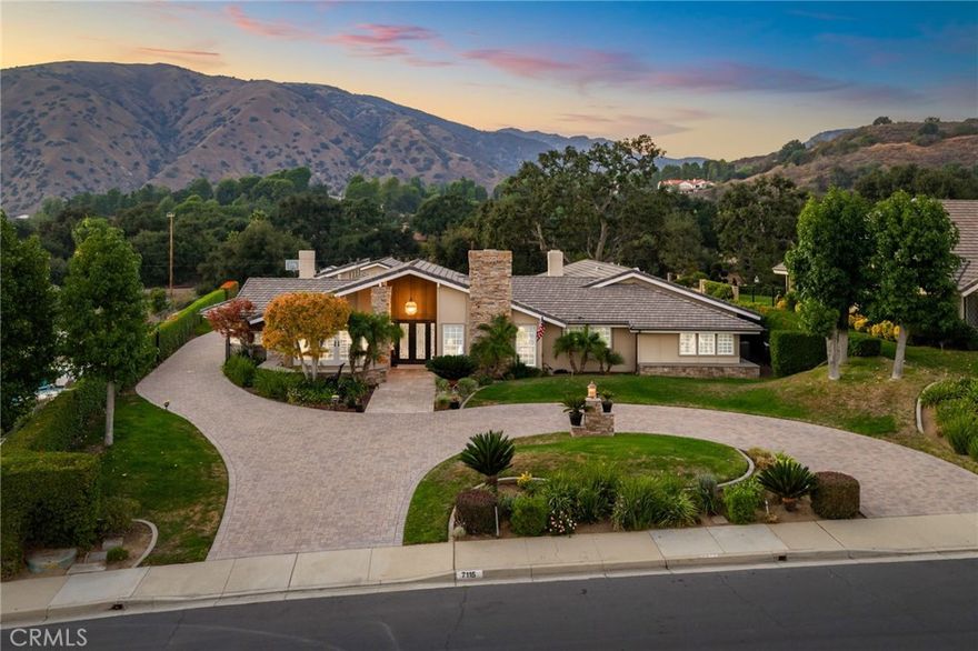 Custom California Ranch-Style Estate featuring a symmetrical façade, circular paver driveway, stacked-stone accents, and meticulous landscaping. Double iron-and-glass entry doors opens to a light-filled interior framed by floor-to-ceiling windows and wood-trimmed architectural columns, leading seamlessly into the formal living and dining rooms. The living room offers a tray ceiling with crown molding, a fireplace, and windows overlooking the front yard. The dining room offers a mirrored coffered ceiling and French doors that open to a front sitting area. The kitchen features custom wood cabinetry, granite countertops, stainless steel appliances, bar-top seating, and a breakfast nook with a built-in desk area. The adjacent family room offers a dramatic fireplace framed in granite, exposed white trusses, and wood-plank ceiling that blends architectural character. French doors and wood-framed, grid-style casement windows provide views and a seamless transition to the backyard. This wing also includes a bathroom with shower, a laundry room, and access to the three-car garage. On the opposite wing, an executive-style office showcases millwork, coffered ceilings, floor-to-ceiling built-ins, and richly stained cabinetry. The luxurious primary suite is a sanctuary–oversized and appointed with tray ceilings, dual sets of French doors, tall windows, and dual walk-in closets. The spa-inspired en suite bath features a jetted tub set beneath stained-glass windows, a walk-in shower, dual vanities with granite counters, and a double-sided fireplace shared with the bedroom. Additional bedrooms include one with an angled tongue-and-groove plank ceiling, and another with a tray ceiling. The hall bathroom features granite countertops, a frameless walk-in shower, and a jetted tub. The private, resort-style backyard is designed for elevated living–an expansive outdoor retreat ideal for entertaining or everyday luxury. A sleek PebbleTec pool is the centerpiece, paired with a stacked-stone spa, dramatic fire bowls, and cascading water features. A covered cabana lounge with vaulted wood ceiling, recessed lighting, heaters, and drapery offers a year-round outdoor living experience. A built-in BBQ island with stainless appliances, a fire table, sail shades, and paver decking sits beneath a majestic oak tree with views of hillside vistas. The detached three-car garage sits beyond a private gated driveway, where a putting green adds the final touch to this extraordinary estate.