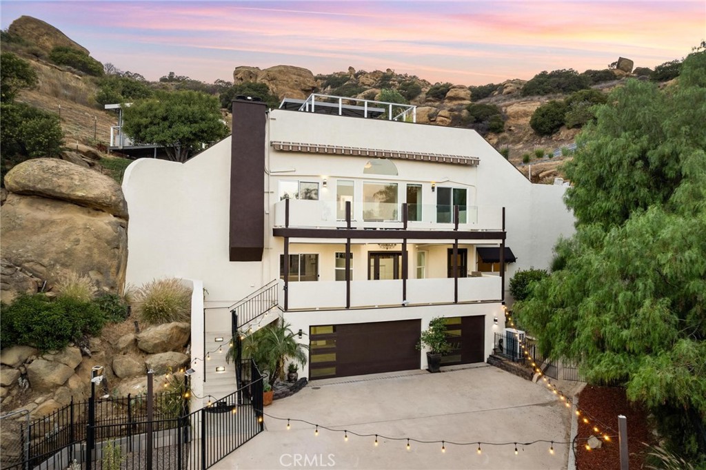 Spectacular Hillside Retreat in Roy Rogers Estates with Panoramic Views. Tucked away behind private gates and set along a scenic driveway, this exceptional property is one of Los Angeles' most distinctive homes. Located in the prestigious Roy Rogers Estates of Chatsworth, this architectural gem is built into the hillside and surrounded by the natural beauty of the Santa Susana Mountains - offering direct access to hiking trails just steps from your front door. The home sits on an expansive 30,000 sq. ft. lot dotted with the dramatic sandstone boulders that define Chatsworth's rugged landscape. Enjoy sweeping views of the Valley from multiple vantage points, including two covered observation decks—one featuring a private spa where you can relax and soak in the scenery. Inside, you'll find a thoughtfully designed layout offering 4 bedrooms, 4 bathrooms and 2,553 sq. ft. of beautifully designed living space, the home features an open-concept layout with a kitchen at its heart—complete with a large island, walk-in pantry, and plenty of space for gathering. A stylish wet bar with a wine refrigerator makes entertaining effortless, while two front-facing balconies offer tranquil Valley views. The accompanying living room boasts a fireplace to relax and take in the surrounding landscape. The spacious primary suite includes a cozy fireplace, a walk-in closet, and a luxurious ensuite bathroom with a soaking tub and separate shower. Additionally, the property features an exterior elevator for easy access to the upper level of the backyard, a spacious 3-car garage, and a fully paid solar energy system. With its blend of seclusion, natural beauty, and modern comforts, this property offers a truly rare opportunity to own a private hillside retreat in one of L.A.’s most coveted hidden enclaves.