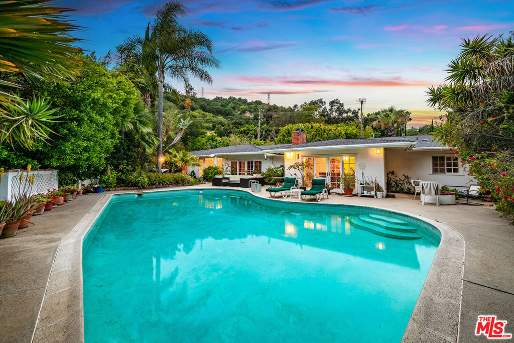 Tucked behind private gates on a lush, approximately one-third-acre lot, this exceptional residence offers 2,433 sqft of elegant living space in the heart of Studio City's prestigious Carpenter Community Charter School district. As you approach the home via a secluded, tree-lined driveway, a sense of peace and privacy takes over. The gated entrance provides off-street parking for multiple vehicles, along with a spacious two-car garage, ensuring both convenience and security. Inside, the home welcomes you with natural light, clean architectural lines, and authentic Spanish tile flooring, all set within a layout that celebrates Mid-Century Modern ideals functionality, indoor-outdoor flow, and built-in design elements. The well-proportioned floor plan offers both connectivity and separation, ideal for today's lifestyle. With three generous bedrooms and a dedicated home office, the layout supports both comfort and creativity. The formal living room radiates character, while the expansive family room, complete with a wet bar and double-sided fireplace, is framed by picture windows that showcase stunning canyon and city views offering a tranquil backdrop whether entertaining or relaxing. Step outside to discover a true resort-style retreat. A very large pool, inviting spa (Jacuzzi), and fire pit anchor the expansive outdoor space, surrounded by mature trees that create a private atmosphere. Multiple patios offer ideal settings for al fresco dining and leisure, including a secluded patio off the primary suite, complete with a soothing fountain a perfect morning or evening escape. Whether you envision a careful restoration, creative update, or full reimagination, this home offers a solid structural foundation and inspiring architectural bones to bring your vision to life.